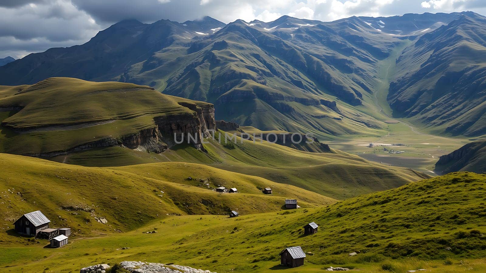 This breathtaking image showcases a stunning mountain landscape, featuring rolling green hills dotted with several rustic wooden cabins. The foreground is dominated by lush pastures, providing a striking contrast to the towering, majestic mountains in the background. These mountains exhibit a beautiful gradient of greens and blues, with hints of snow visible on the higher peaks. The partially cloudy sky adds depth and drama to the scene, highlighting the textures and colors of the landscape. This image is perfect for projects related to travel, nature, adventure, tourism, and real estate, particularly those emphasizing eco-tourism or sustainable living in scenic locations. The sense of serenity and untouched beauty makes it ideal for calendars, brochures, websites, and other media seeking to convey a message of tranquility and escape.