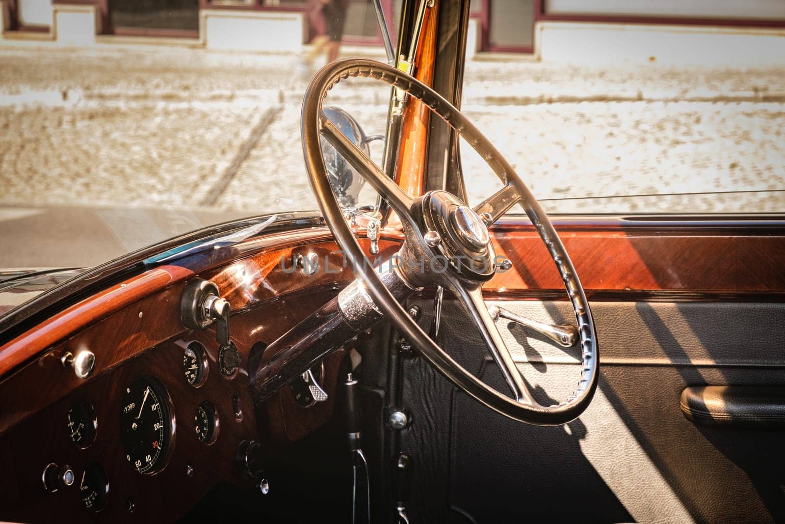 Lisbon, Portugal - Sep 29, 2024: Close-up and selective focus on vintage luxury 1937 Rolls-Royce Phantom III interior. Steering wheel and dashboard in wood, leather and chrome lit by sunlight.