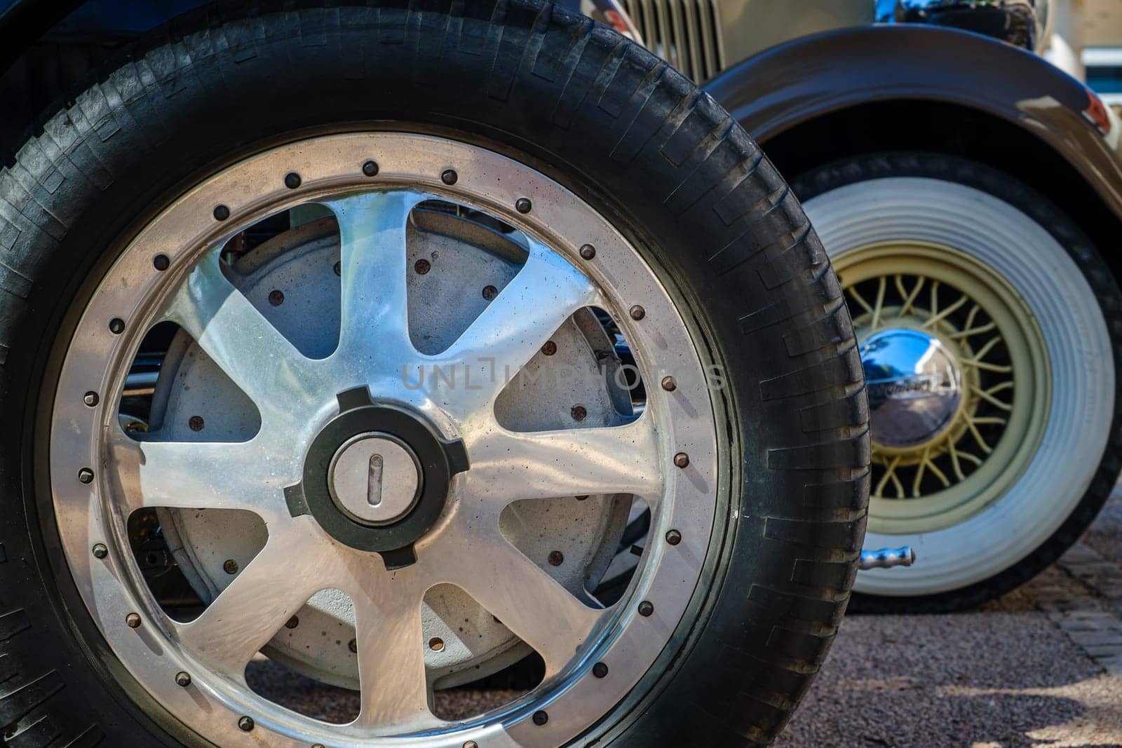 Lisbon, Portugal - Sep 29, 2024: Vintage car wheels on cobblestone road. Wheel design, wire wheel with white wall rubber tyre, chrome polished center hub cap and traditional spokes, cast aluminum racing wheel with central locking hub, 6-spoke design