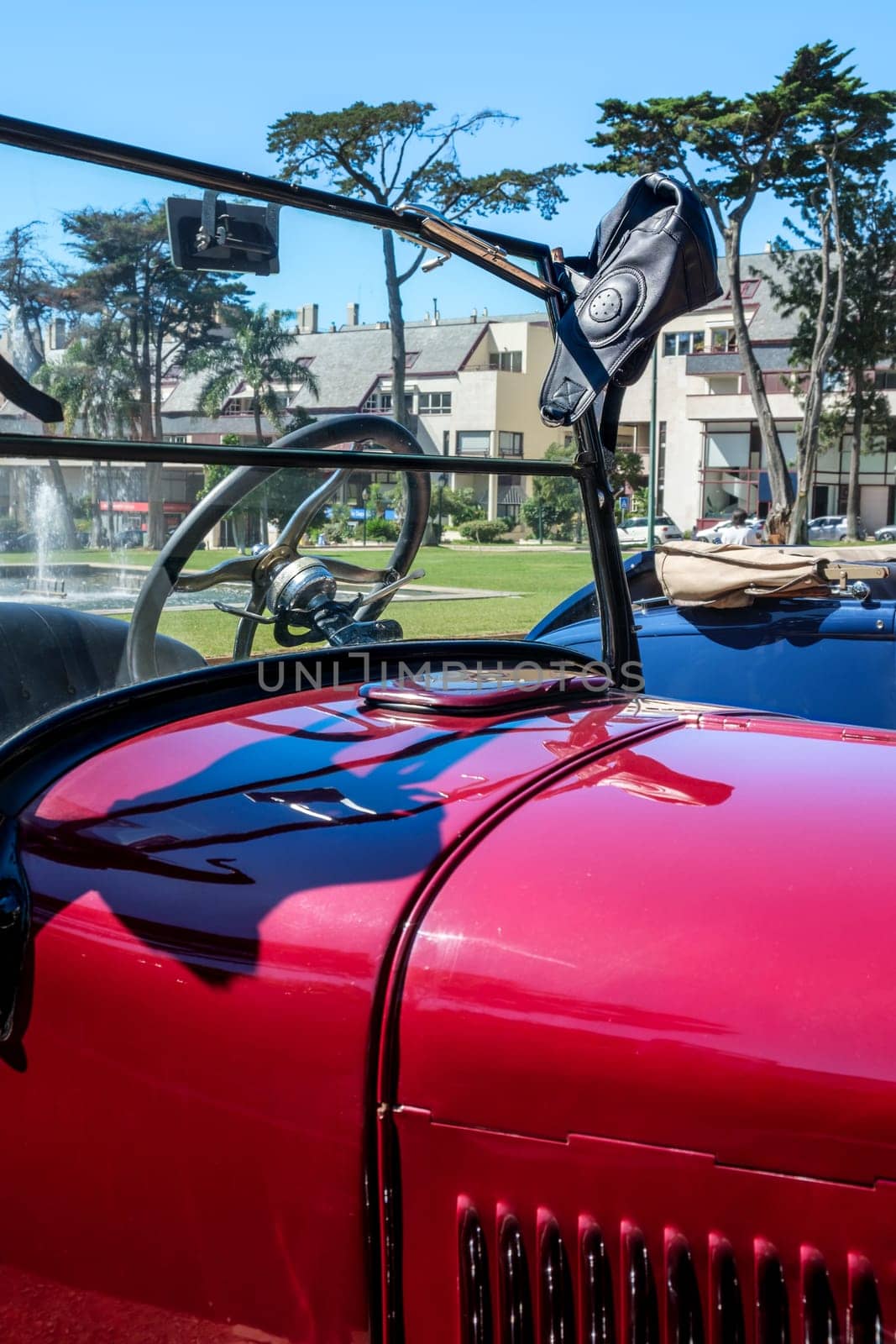 Lisbon, Portugal - Sep 29, 2024: Windscreen and hood of classic Ford Model A or A-Model Ford or the A and A-bone in original red color with a leather aviator helmet hanging on edge of windshield frame on sunny day.