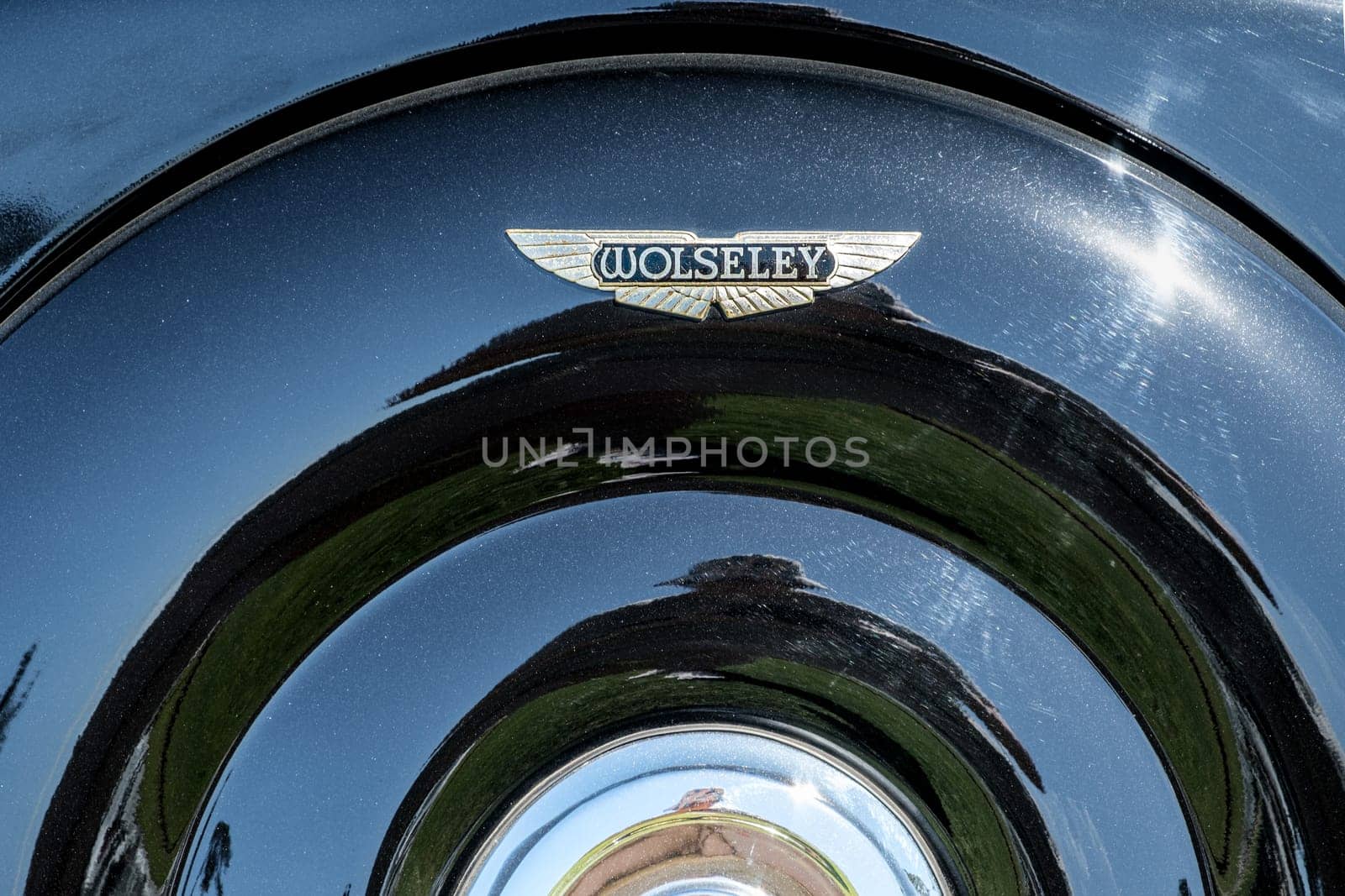 Lisbon, Portugal - Sep 29, 2024: Close-up of vintage Wolseley car spare wheel cover, metal case and Wolseley winged logo badge on sunny day. Sunlight, sun flares, reflections on clean black polished surface. Wolseley, UK