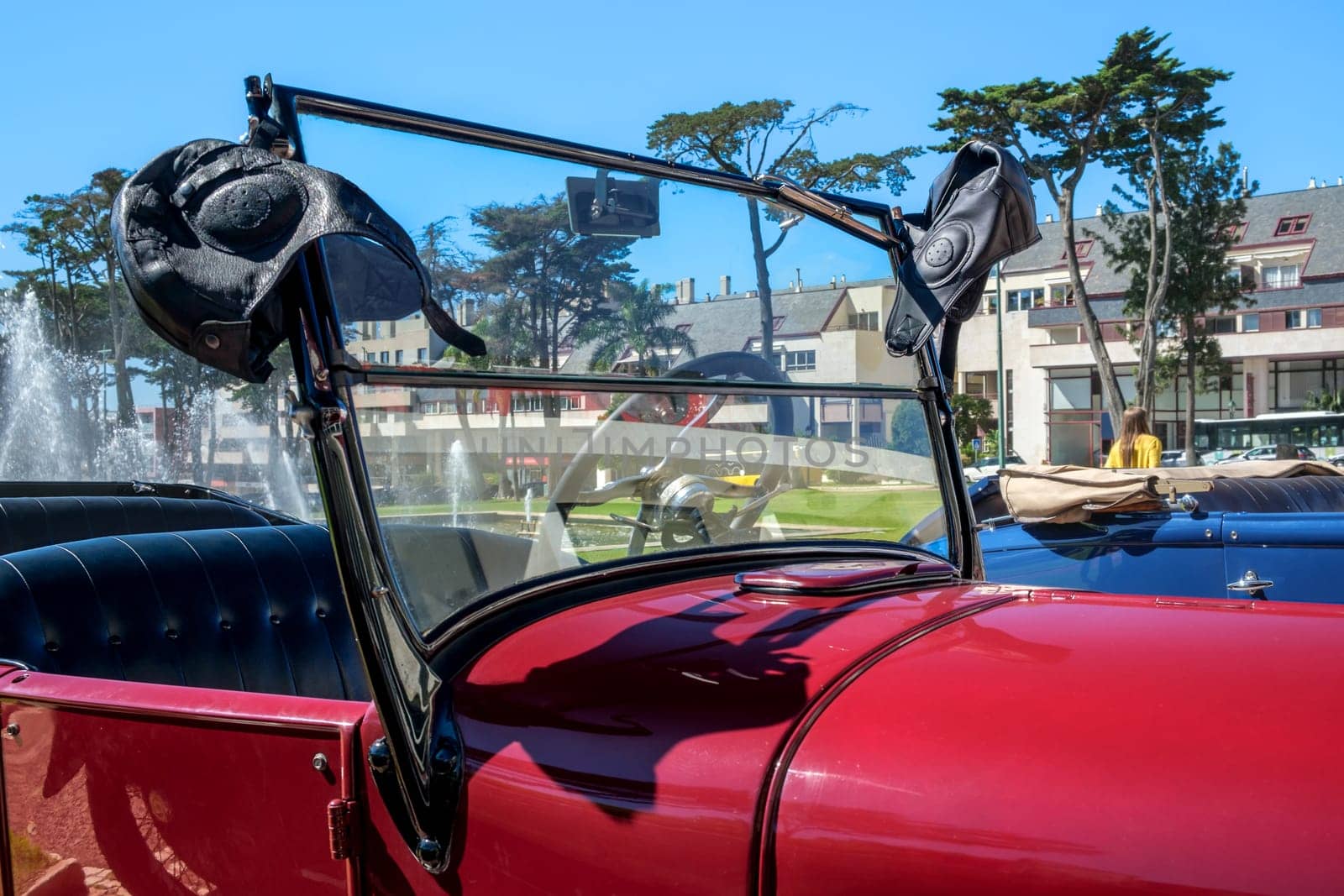 Lisbon, Portugal - Sep 29, 2024: Windscreen and hood of classic Ford Model A or A-Model Ford or the A and A-bone in original red color with two leather aviator helmets hanging on edge of windshield frame on sunny day. Soft top down, car seats visible