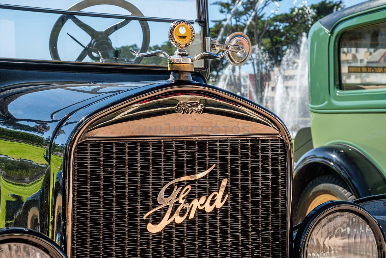Lisbon, Portugal - Sep 29, 2024: Close-up and selective focus on the Boyce MotoMeter on top of hood or bonnet and Ford emblem and logo plate on grille, Ford model T, sunny day, clear blue sky. Ford Motor Company, USA