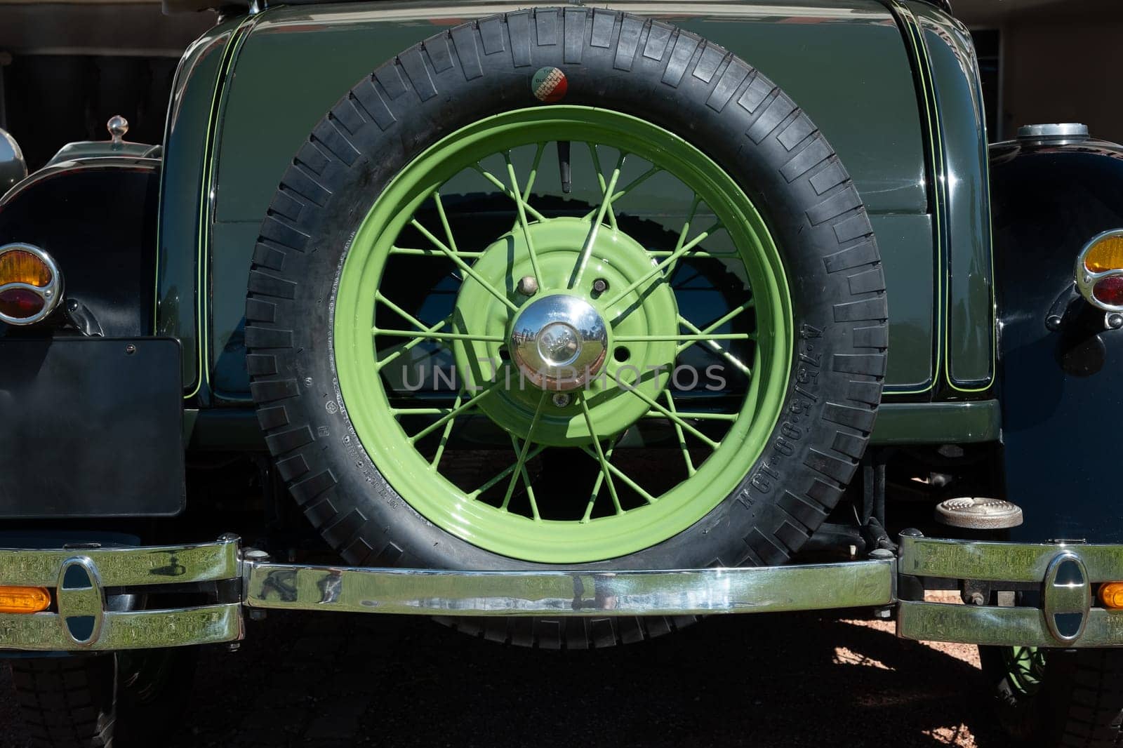 Lisbon, Portugal - Sep 29, 2024: Close view of Ford Model A or A-Model Ford or the A, and A-bone spare wheel attached to trunk on sunny day. Wire wheel chrome details with sun flares, iconic Ford lettering trademark on wheel spinner cap.