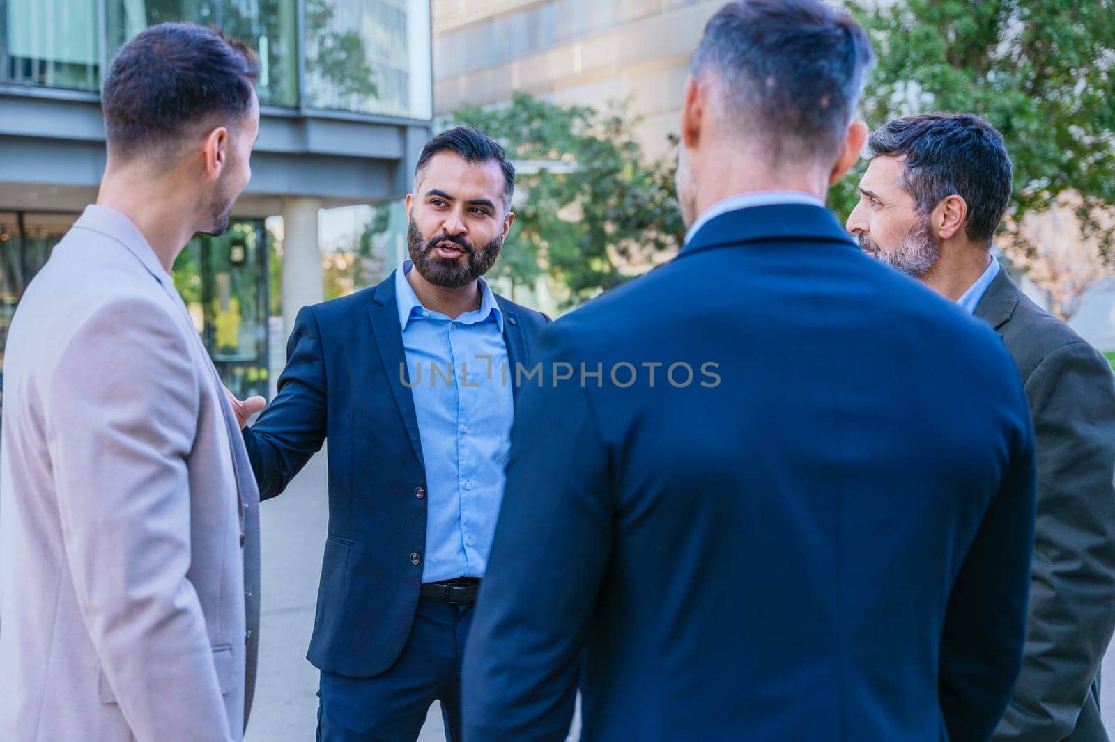 A group of business professionals engaged in a serious discussion outdoors. They are dressed in formal and smart casual attire, with a modern cityscape in the background.
