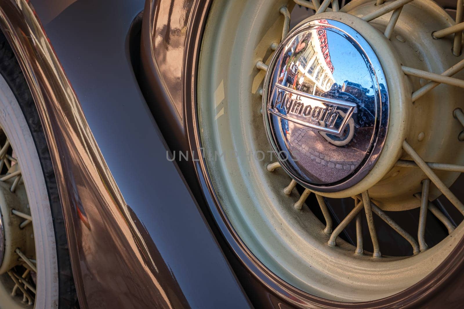 Lisbon, Portugal - Sep 29, 2024: Close-up and selective focus of spare wire wheel and wheel center cap with Plymouth logo on sunny day. Urban setting reflections, vintage look. Plymouth Chrysler motors, Chrysler Corp, USA