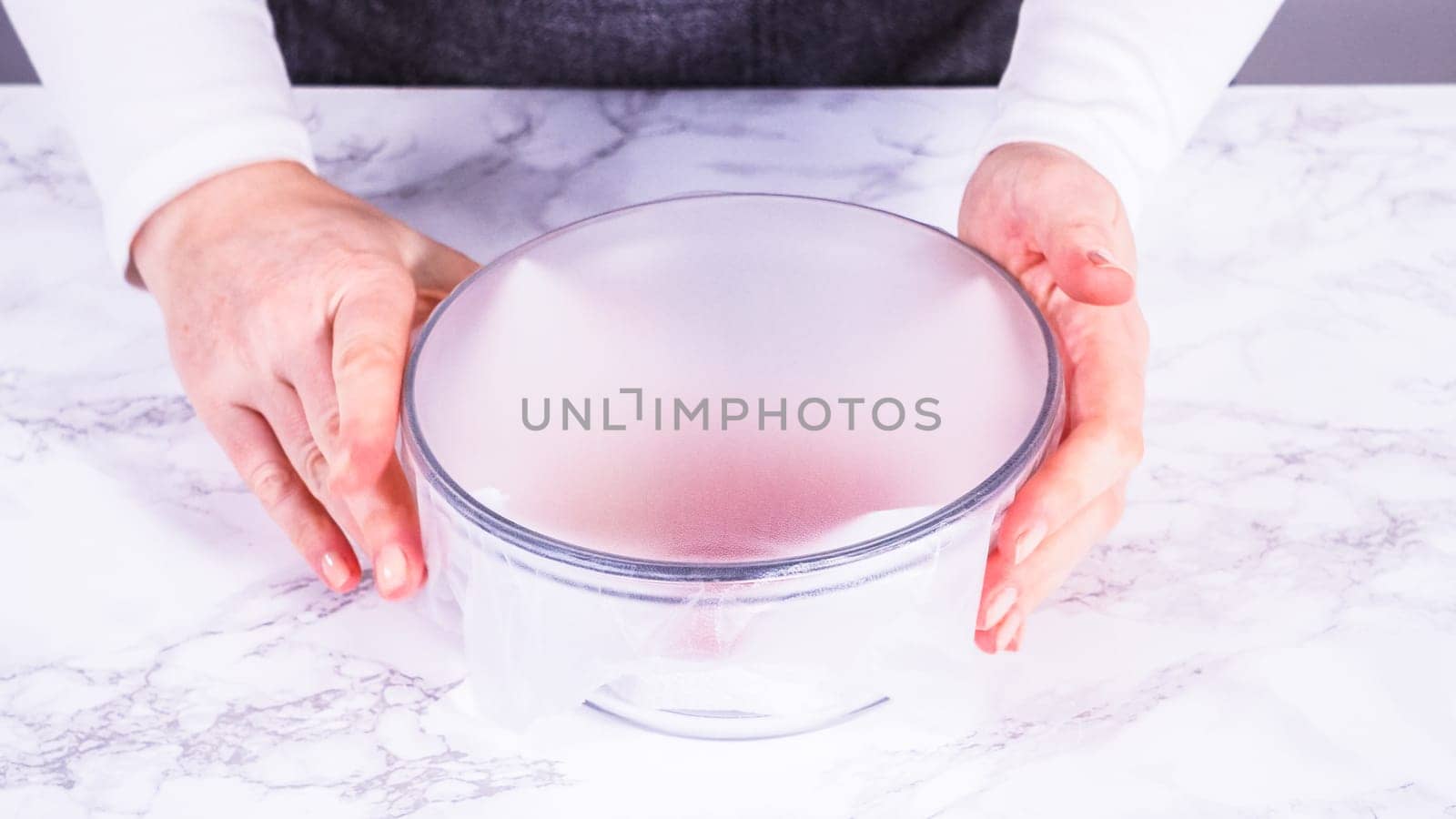 Strawberries, freshly washed and dried, are neatly stored in a glass bowl lined with a paper towel and securely covered with plastic wrap to maintain freshness.