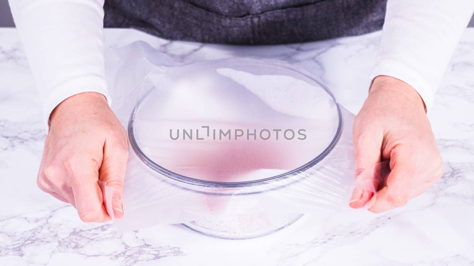 Strawberries, freshly washed and dried, are neatly stored in a glass bowl lined with a paper towel and securely covered with plastic wrap to maintain freshness.