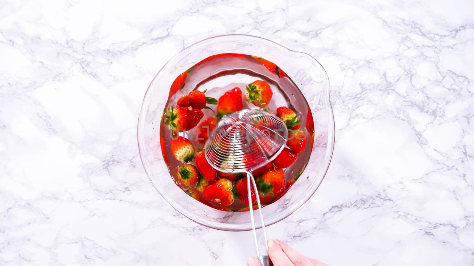 Flat lay. Ripe strawberries are submerged in water within a large glass mixing bowl, a step in washing the fruit to ensure cleanliness and longevity before storage or consumption.