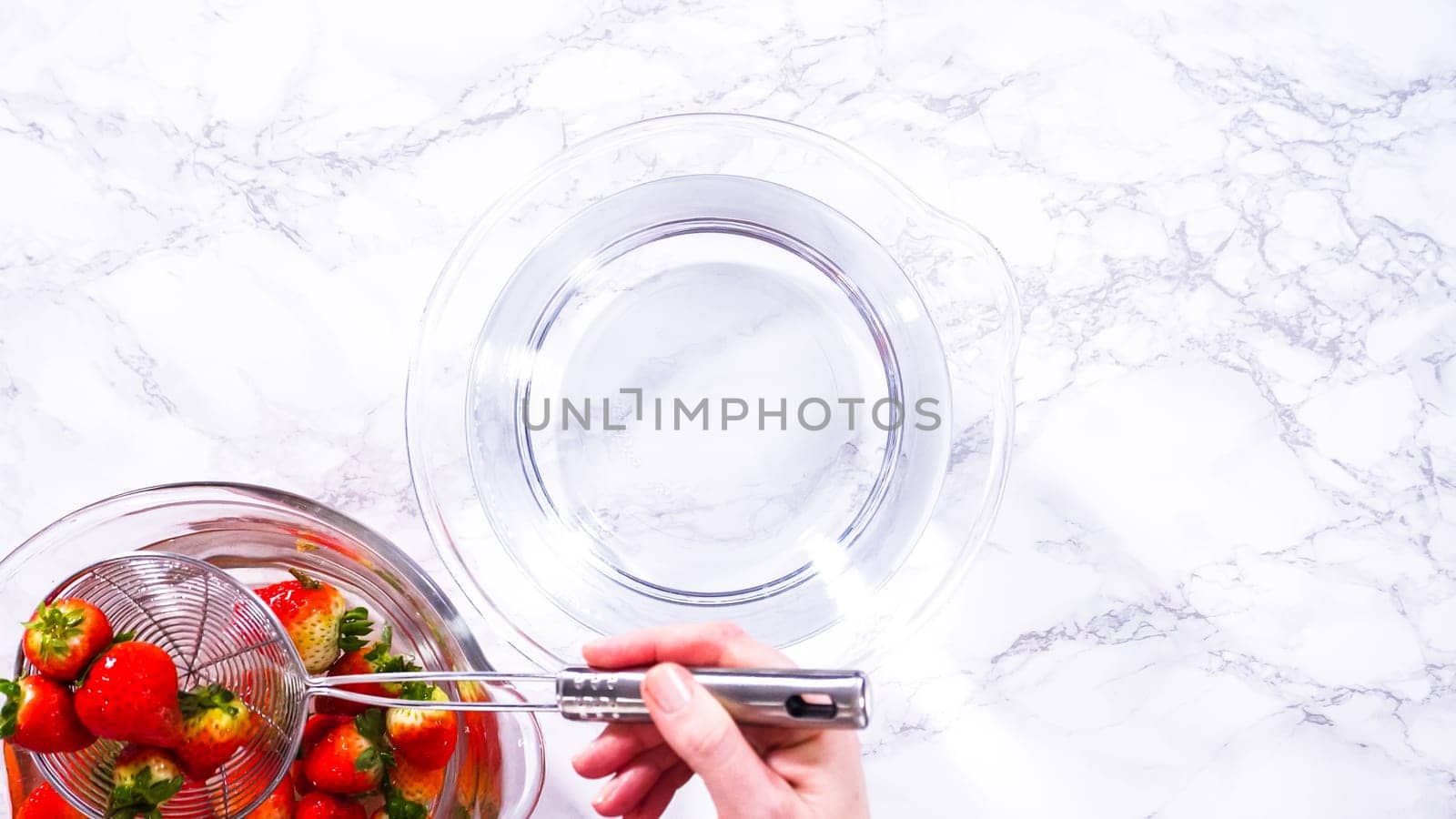 Flat lay. Ripe strawberries are submerged in water within a large glass mixing bowl, a step in washing the fruit to ensure cleanliness and longevity before storage or consumption.