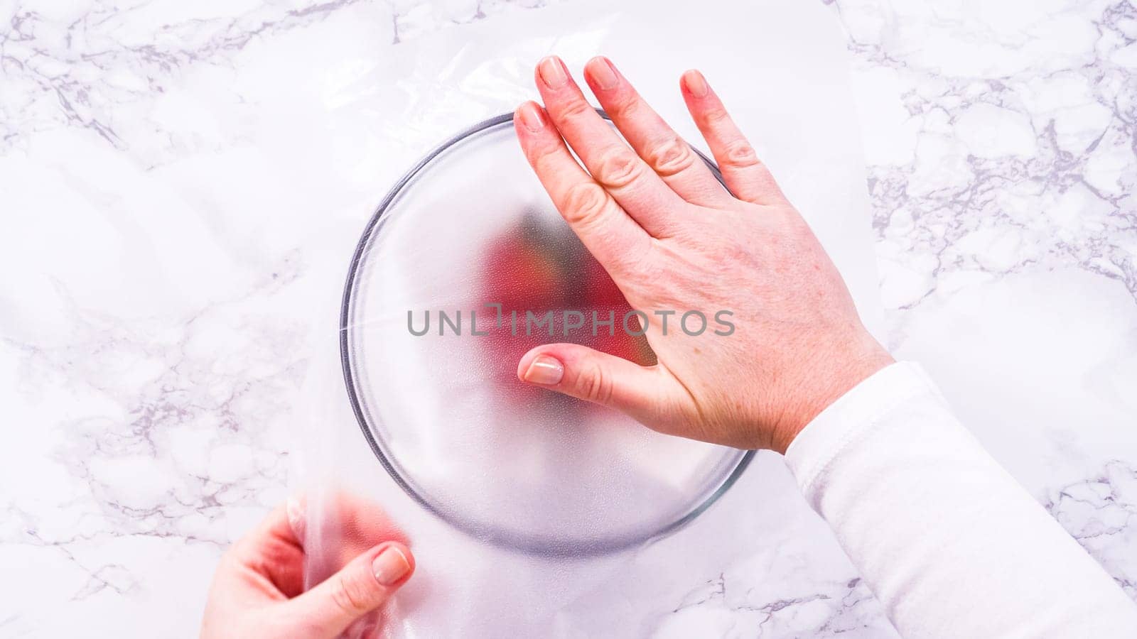 Flat lay. Strawberries, freshly washed and dried, are neatly stored in a glass bowl lined with a paper towel and securely covered with plastic wrap to maintain freshness.