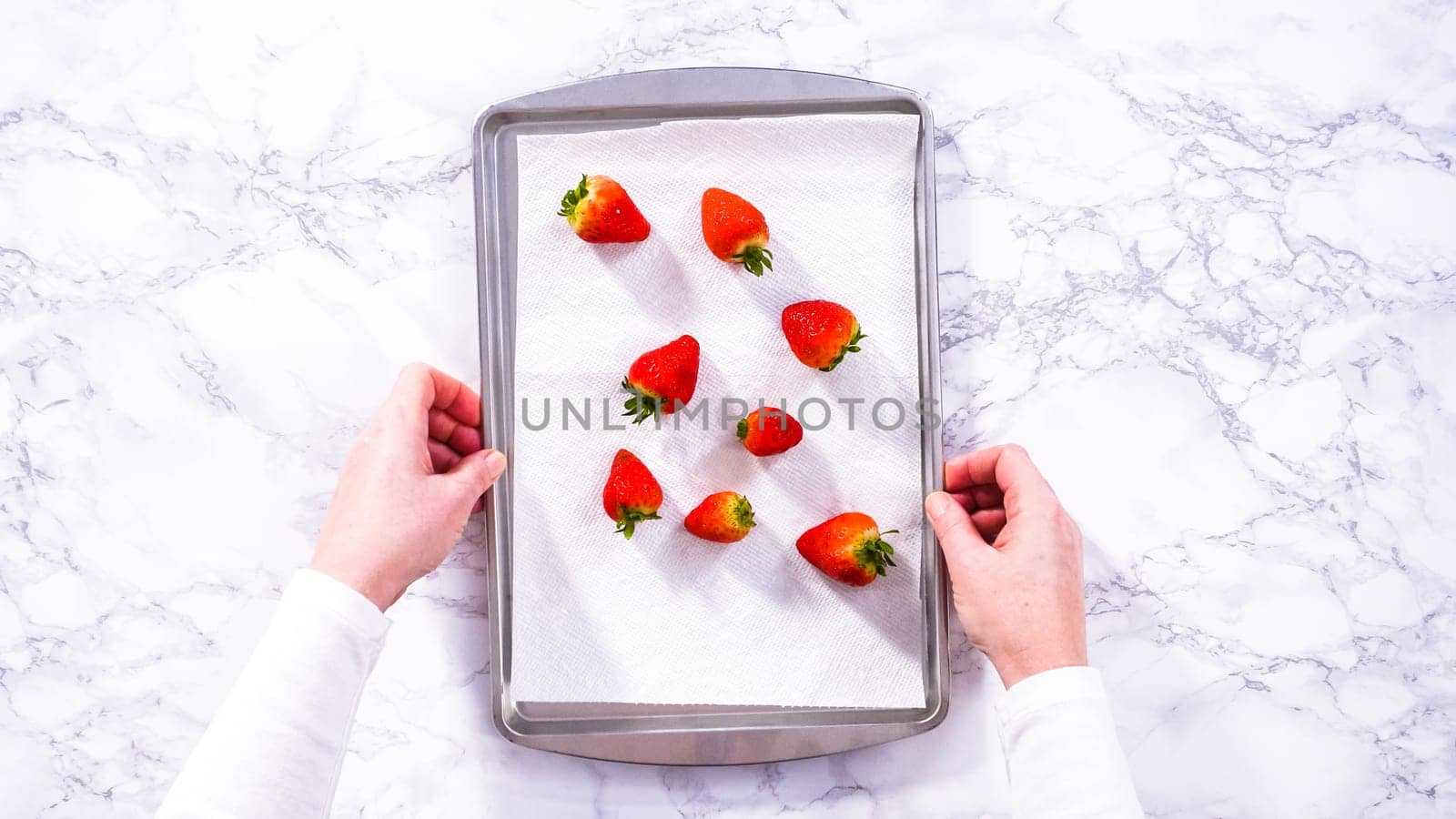 Flat lay. Juicy red strawberries, freshly washed, are spread out to dry on a baking sheet, carefully lined with paper towels to absorb excess moisture and prevent mold.