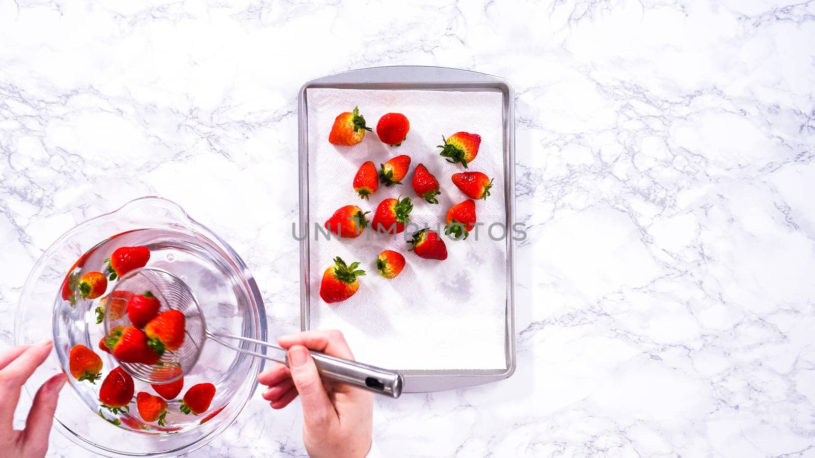 Flat lay. Juicy red strawberries, freshly washed, are spread out to dry on a baking sheet, carefully lined with paper towels to absorb excess moisture and prevent mold.