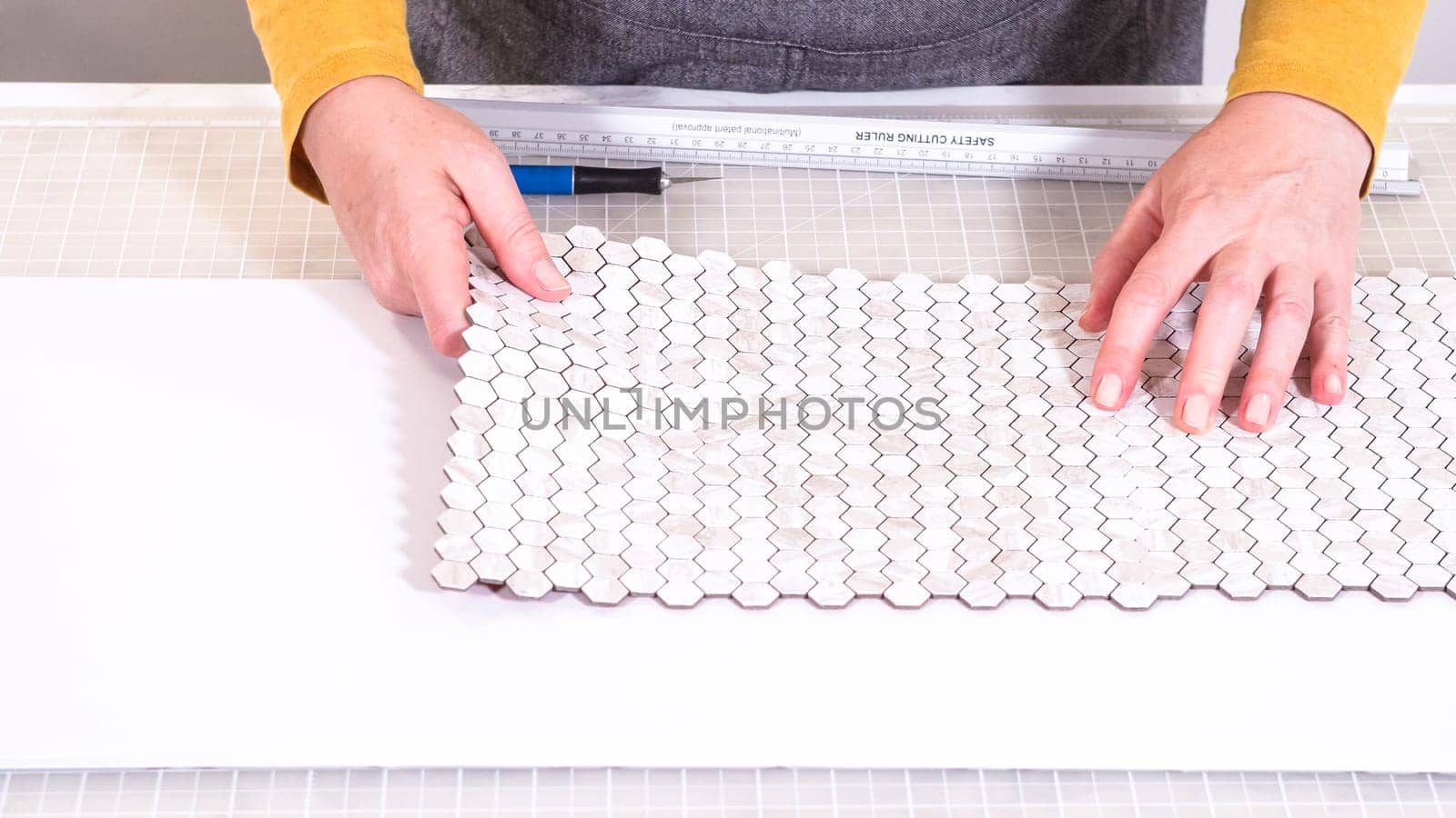 In the process of mounting peel and stick mosaic tiles onto a foam board, perfect for enhancing a food photography studio's aesthetic.
