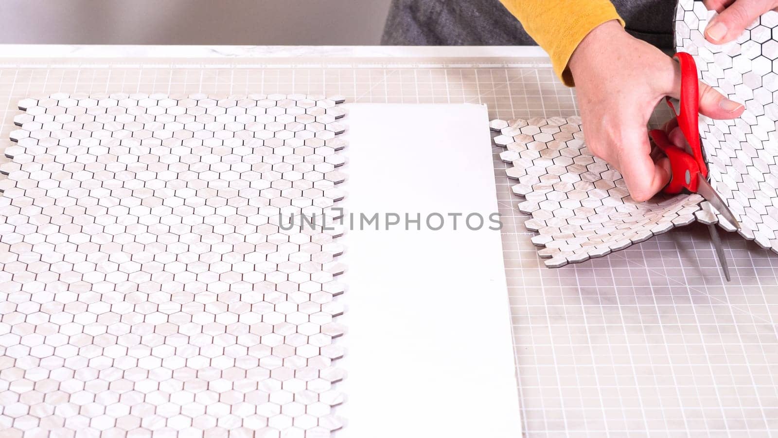 In the process of mounting peel and stick mosaic tiles onto a foam board, perfect for enhancing a food photography studio's aesthetic.