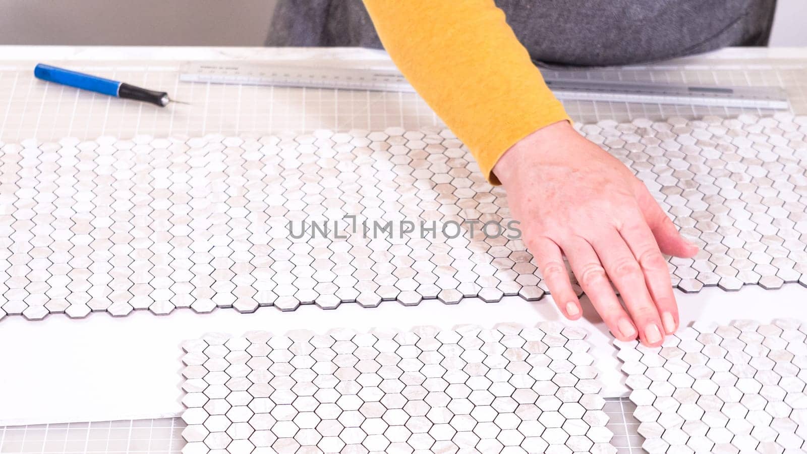 In the process of mounting peel and stick mosaic tiles onto a foam board, perfect for enhancing a food photography studio's aesthetic.