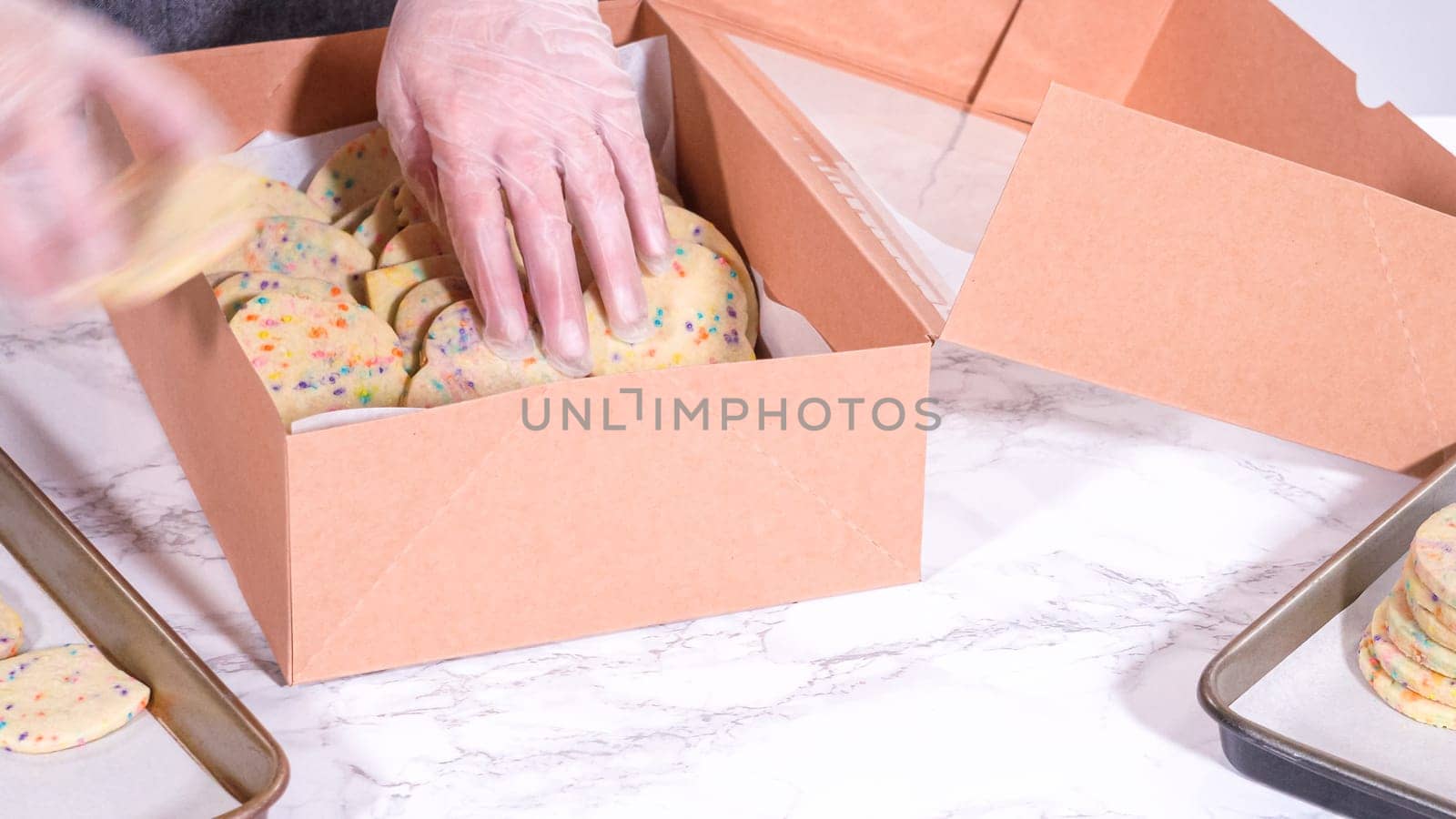 The sugar cookies, filled with sprinkles mixed into the dough, are carefully arranged with meticulous precision into a rustic brown paper box.