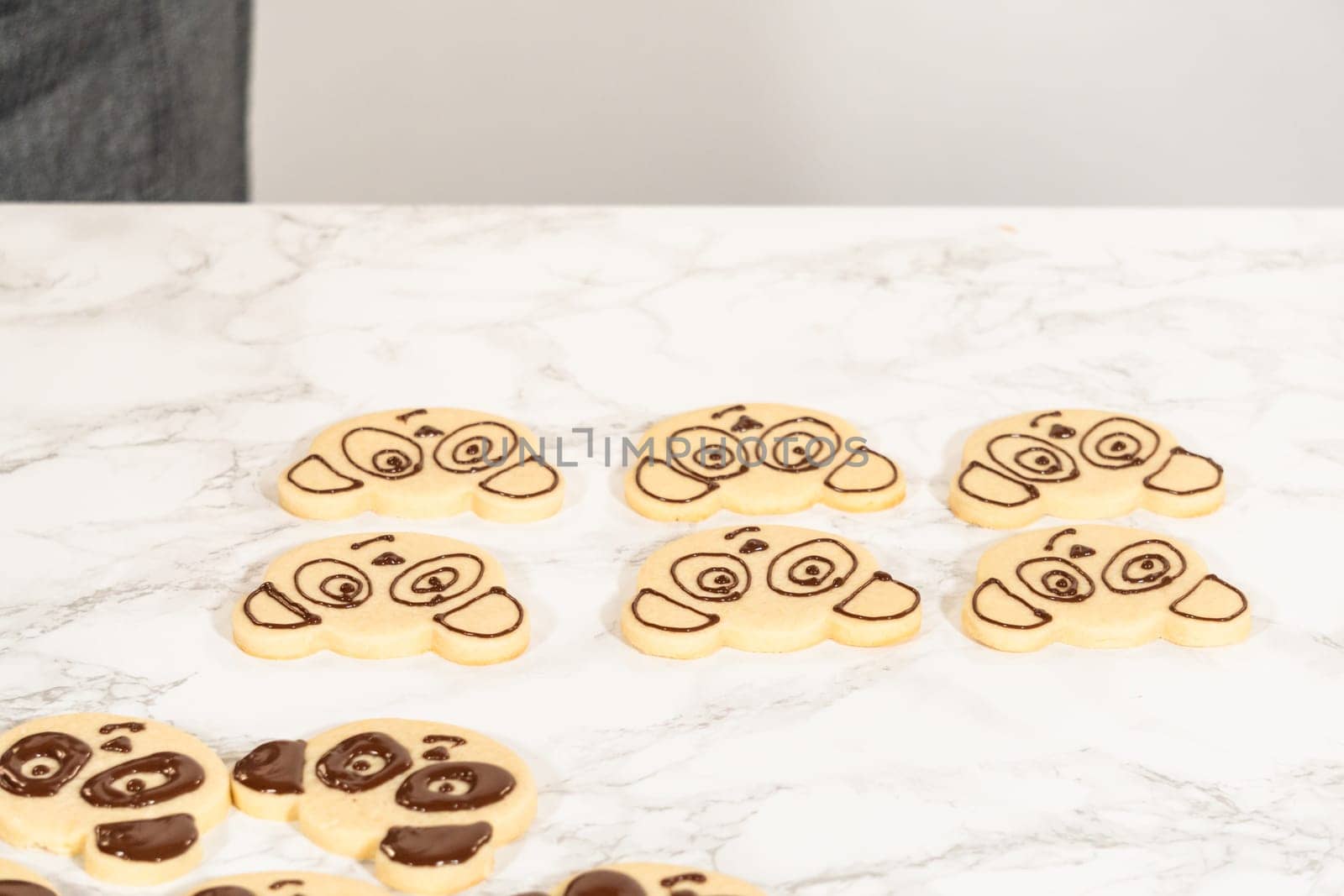 Full Batch of Panda Face Cookies Description: Front view of a full batch of decorated panda face cookies arranged on a marble surface, each detailed with chocolate royal icing for eyes, ears, and nose.