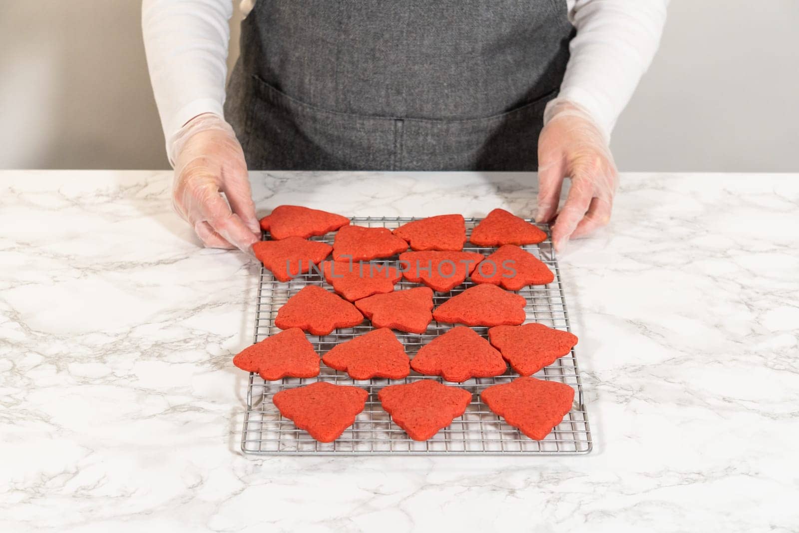 A cooling rack filled with red, tree-shaped gingerbread cookies, freshly baked and arranged in rows. These Red Gingerbread Cookies are cooling on the counter, showcasing their vibrant color and festive shapes.