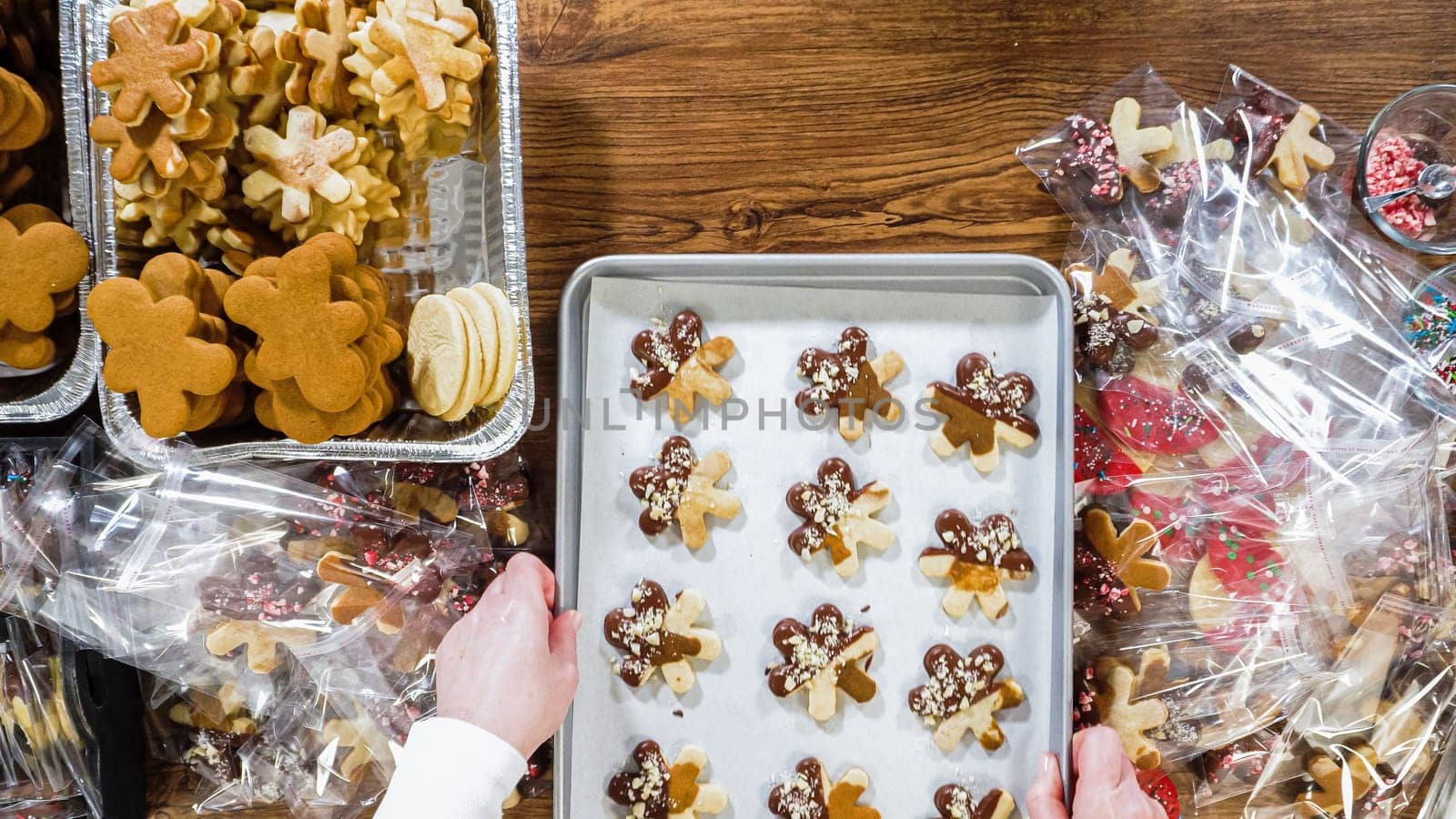 Flat lay. Carefully packaging Christmas cutout cookies, half-dipped in chocolate, sprinkled with crushed nuts, and presented in clear cellophane wrapping.