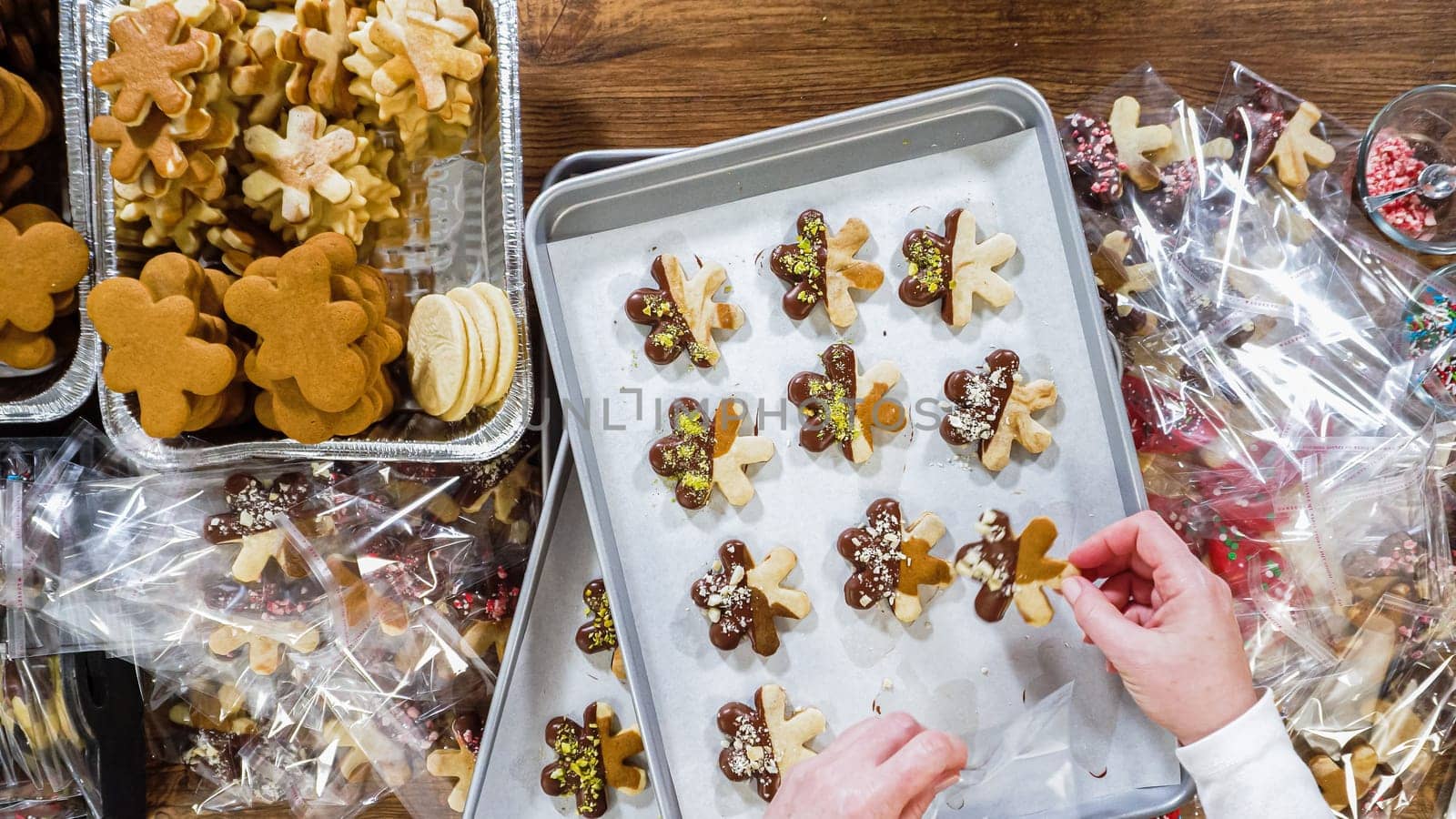Flat lay. Carefully packaging Christmas cutout cookies, half-dipped in chocolate, sprinkled with crushed nuts, and presented in clear cellophane wrapping.