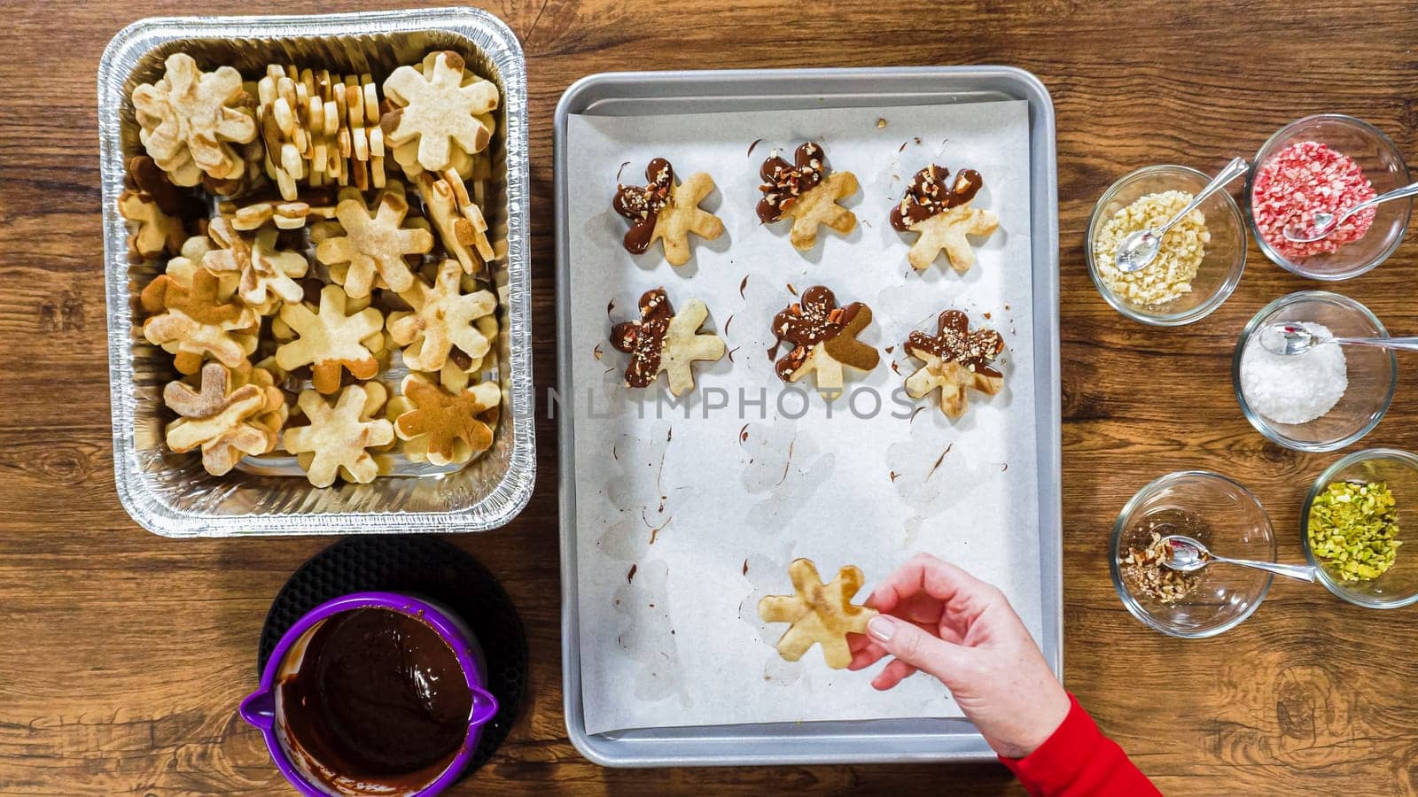 Flat lay. Creating snowflake-shaped cutout sugar cookies, dipped in chocolate, and adorned with different toppings.