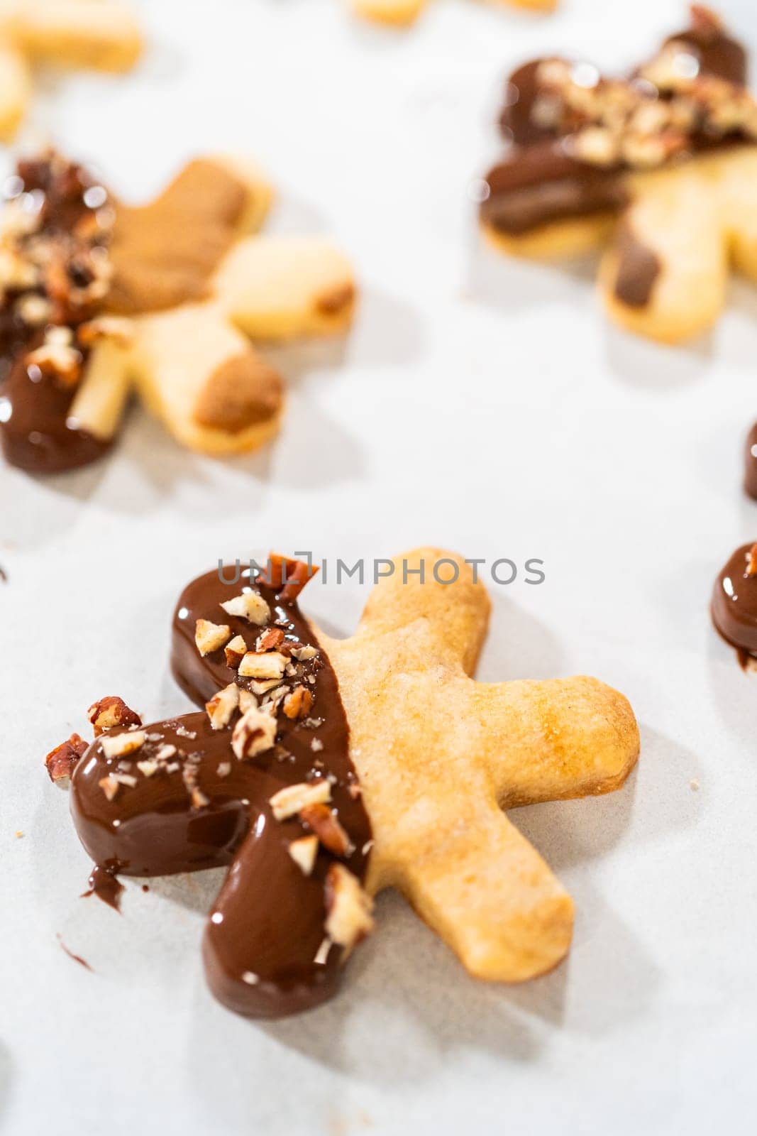 Creating snowflake-shaped cutout sugar cookies, dipped in chocolate, and adorned with crushed pecan nuts, elegantly presented on parchment.