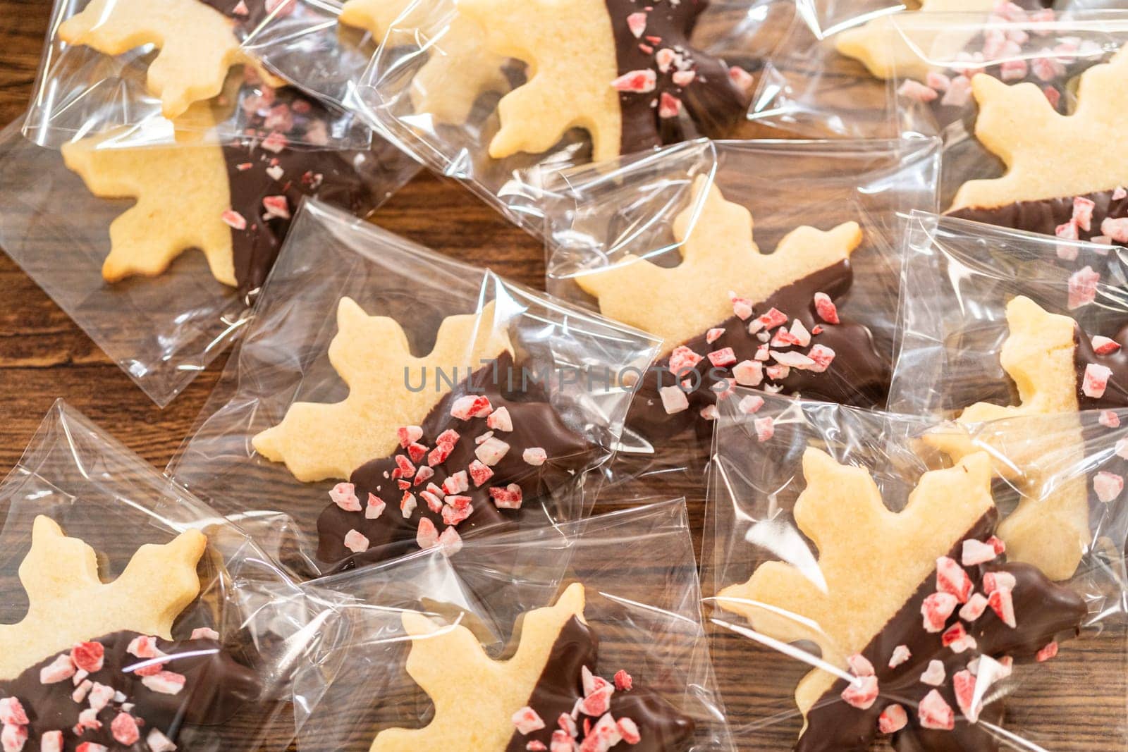 Carefully packaging Christmas cutout cookies, half-dipped in chocolate and presented in clear cellophane wrapping, perfect for festive gifting.