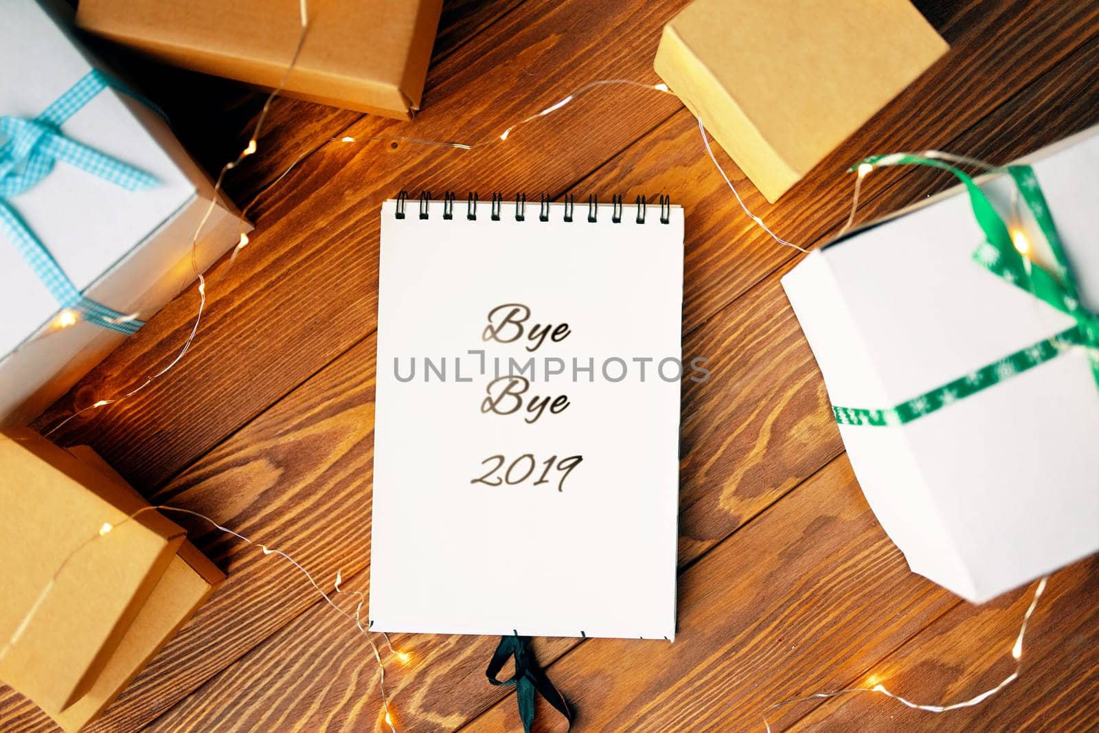 Prepare for Christmas with Notepad and gifts. Notebook with the words Bye Bye 2019 lies on a wooden table.