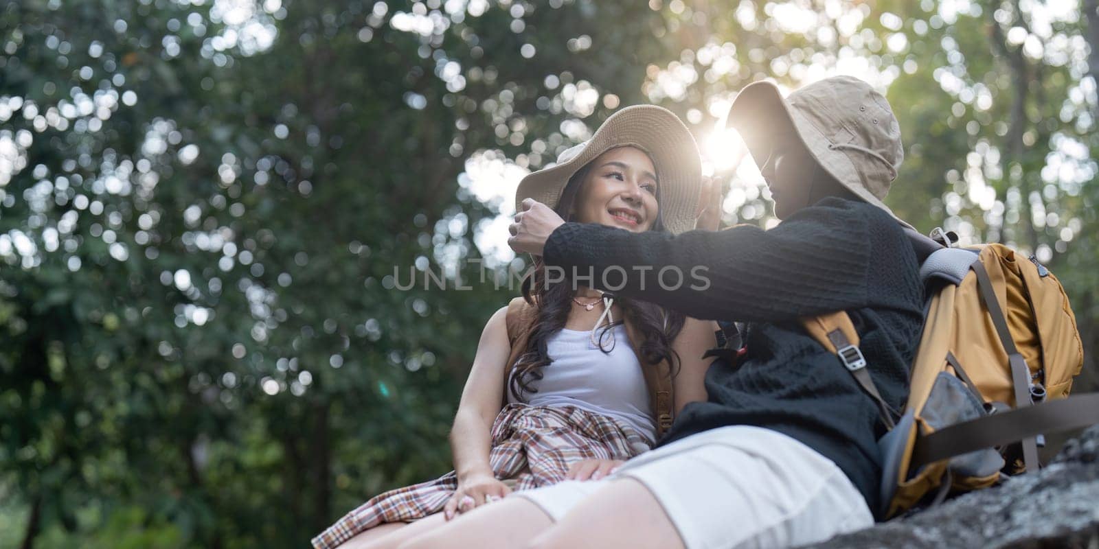 Two women, a loving couple, sitting closely on a rock, smiling at each other as they enjoy their hiking adventure in a beautiful, sun drenched natural setting.
