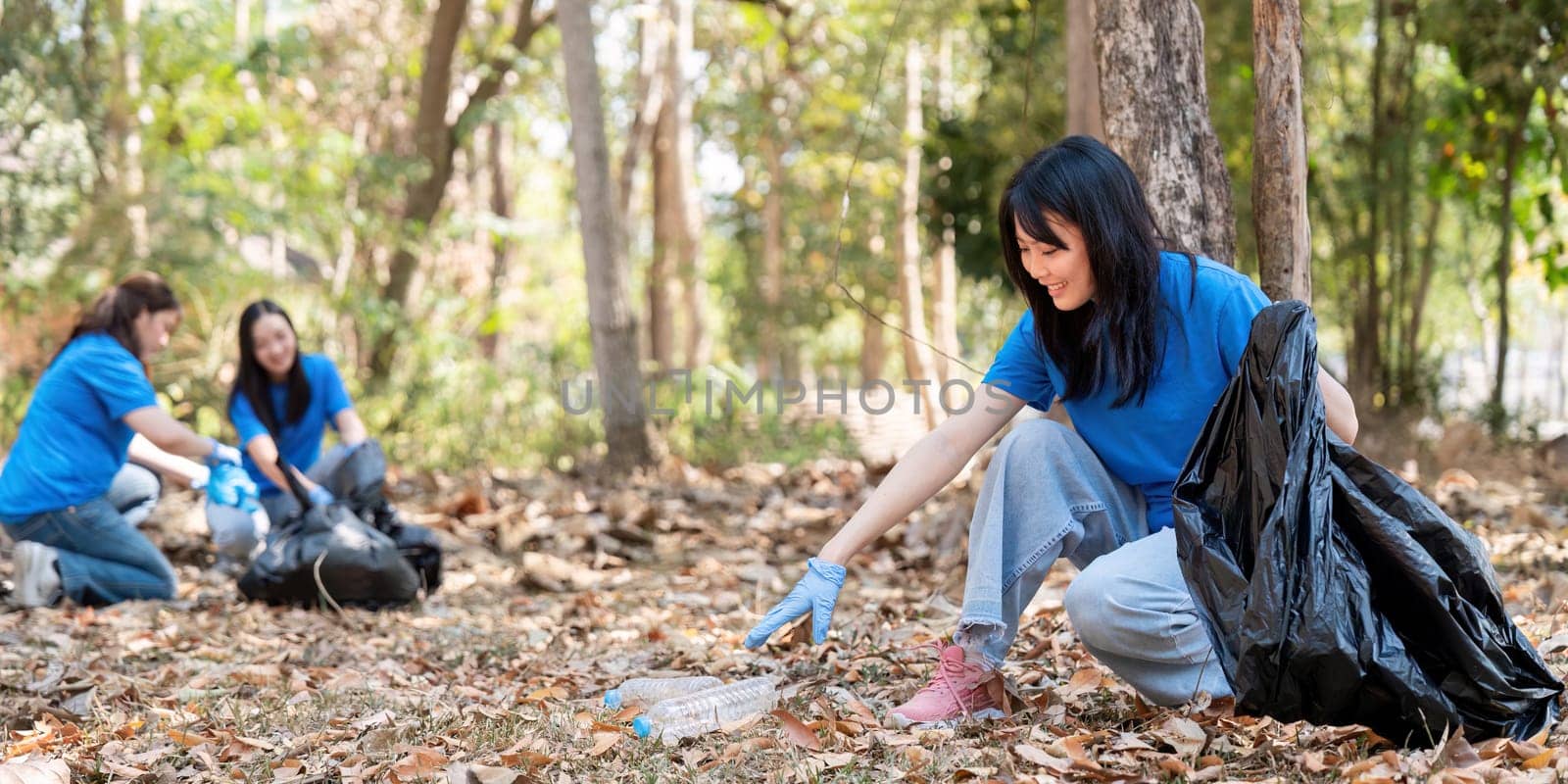 A group of young women in blue shirts actively picking up litter in a park, demonstrating teamwork and commitment to a cleaner environment.
