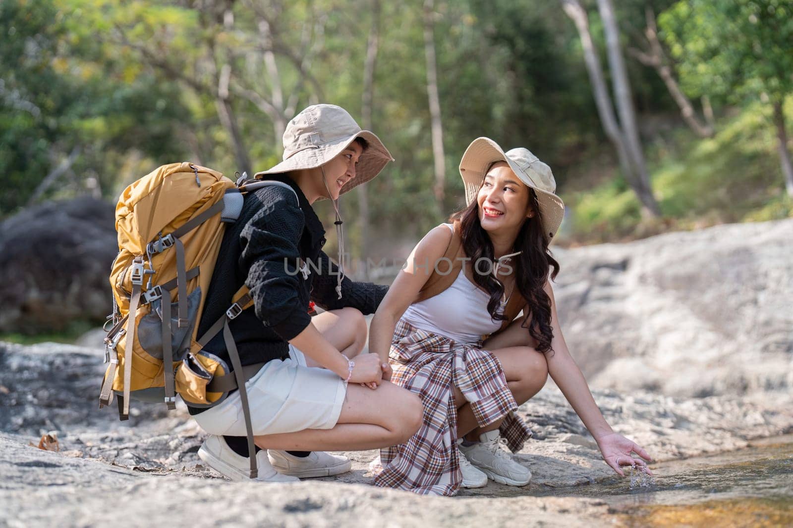 Two women, a loving couple, exploring the outdoors together, laughing and playing by a peaceful stream while hiking in a beautiful natural setting.