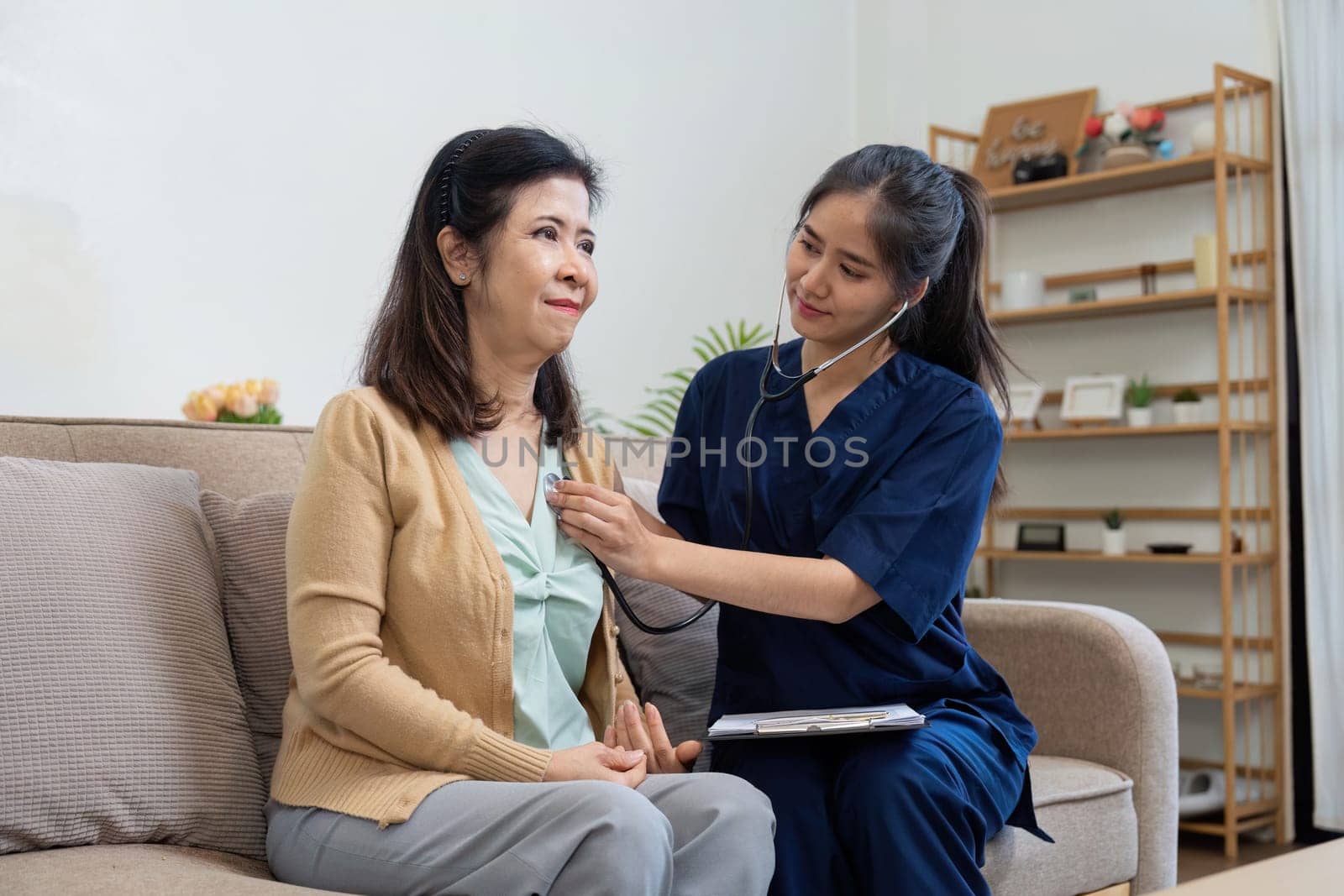 A caregiver attentively listens to the heartbeat of an elderly woman with a stethoscope, showcasing the importance of regular health assessments in a comfortable environment.