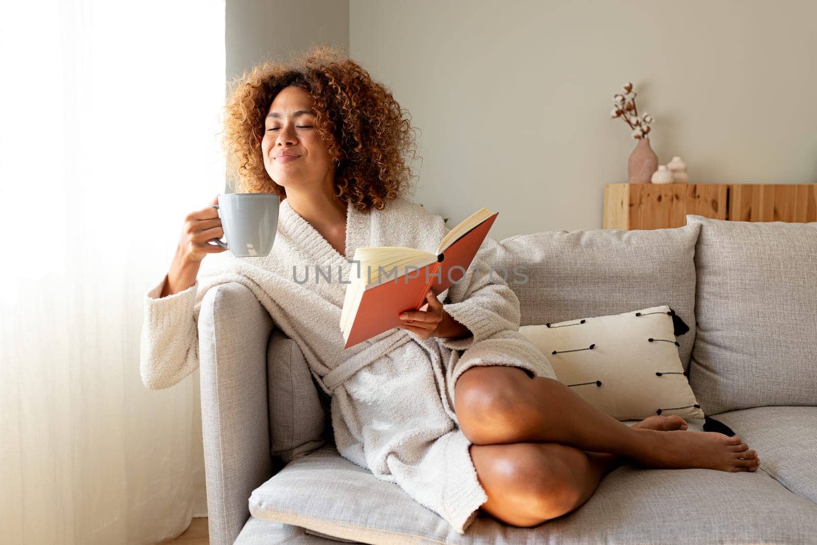 Pensive relaxed Multiracial hispanic woman looking while holding a book and a coffee sitting on the couch Lifestyle concept.