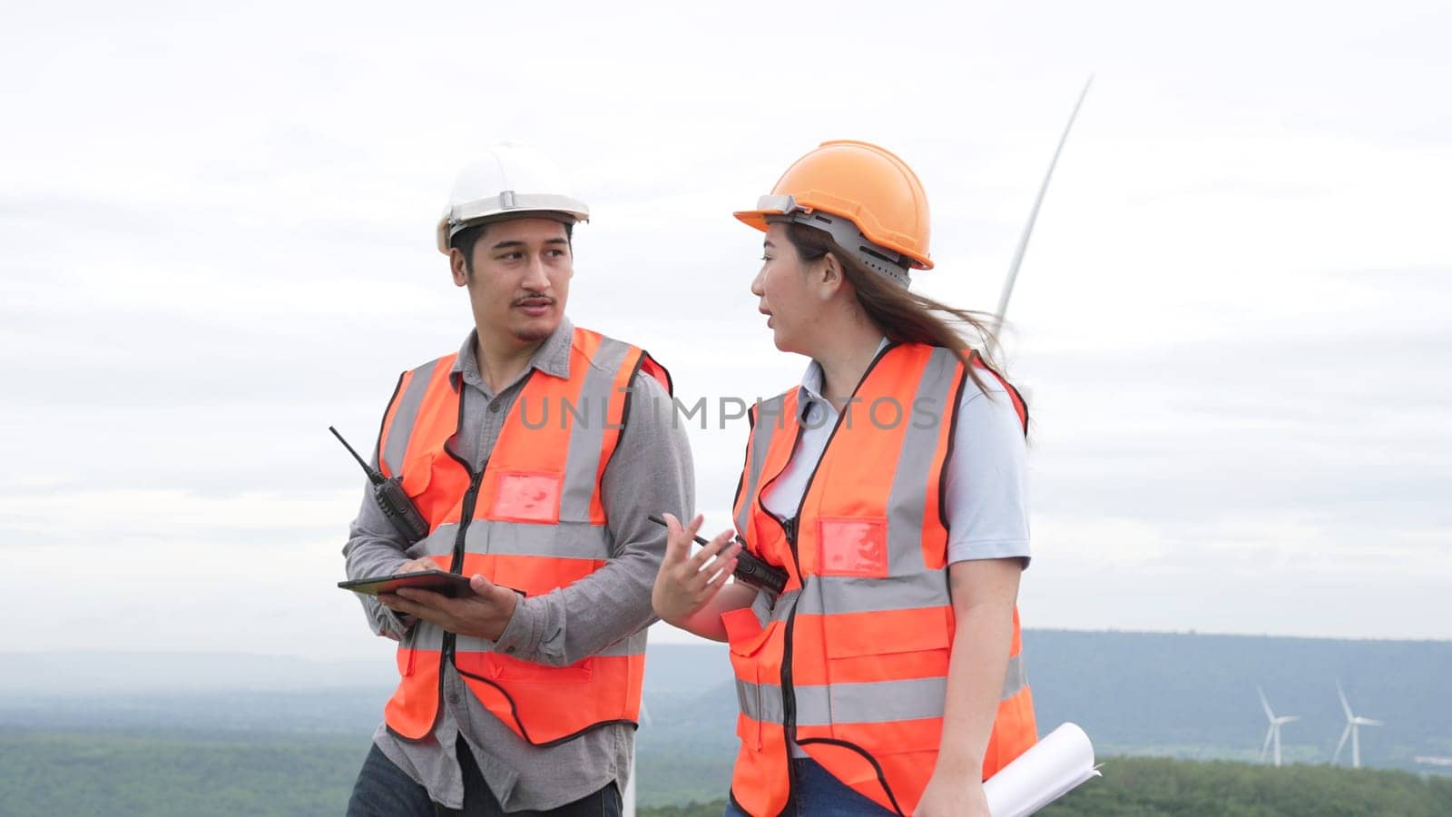 Male and female engineers working on a wind farm atop a hill or mountain in the rural. Progressive ideal for the future production of renewable, sustainable energy.