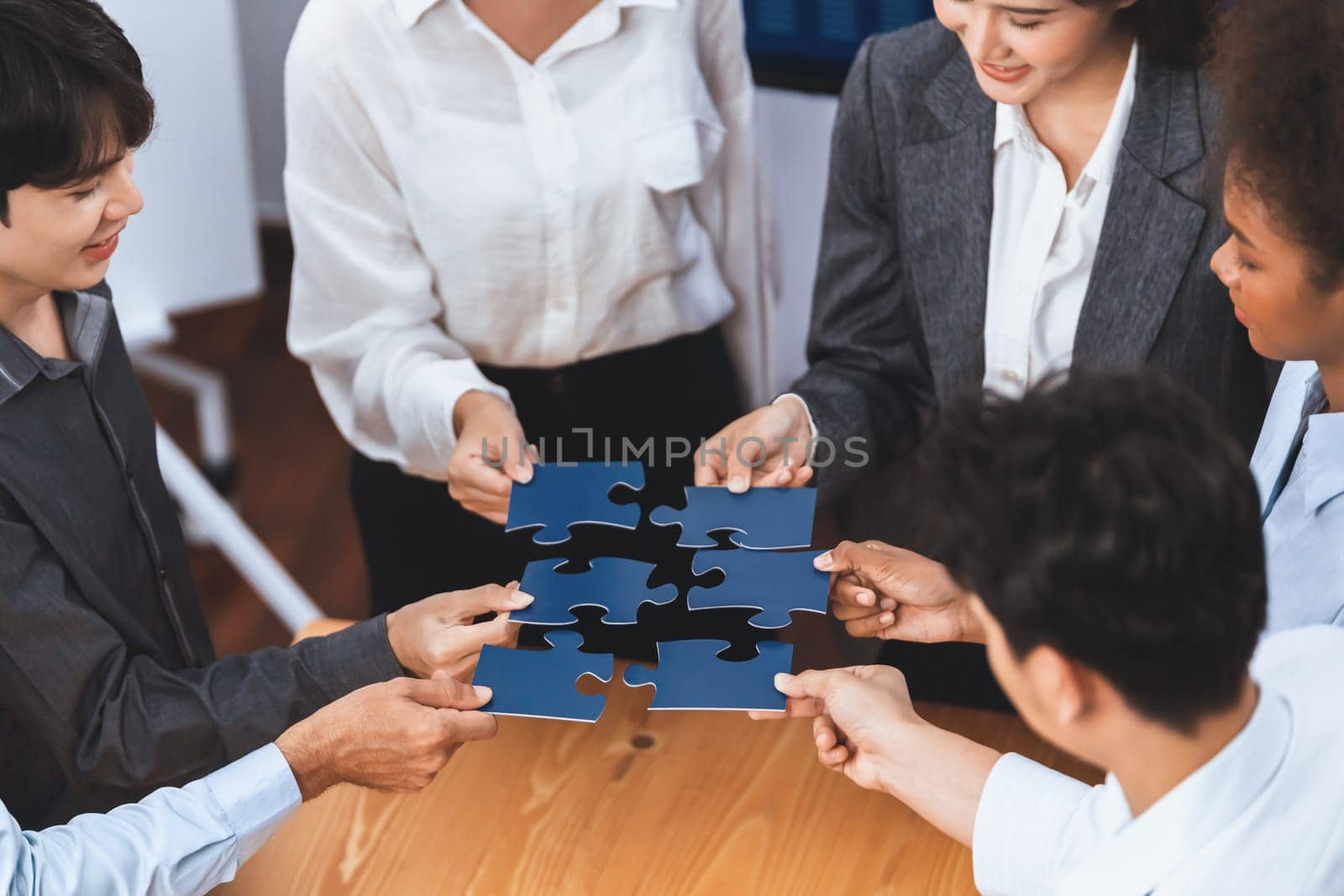 Corporate officer worker collaborate in office, connecting puzzle pieces with report paper on table as partnership and teamwork. Unity and synergy in business concept by merging jigsaw puzzle. Concord