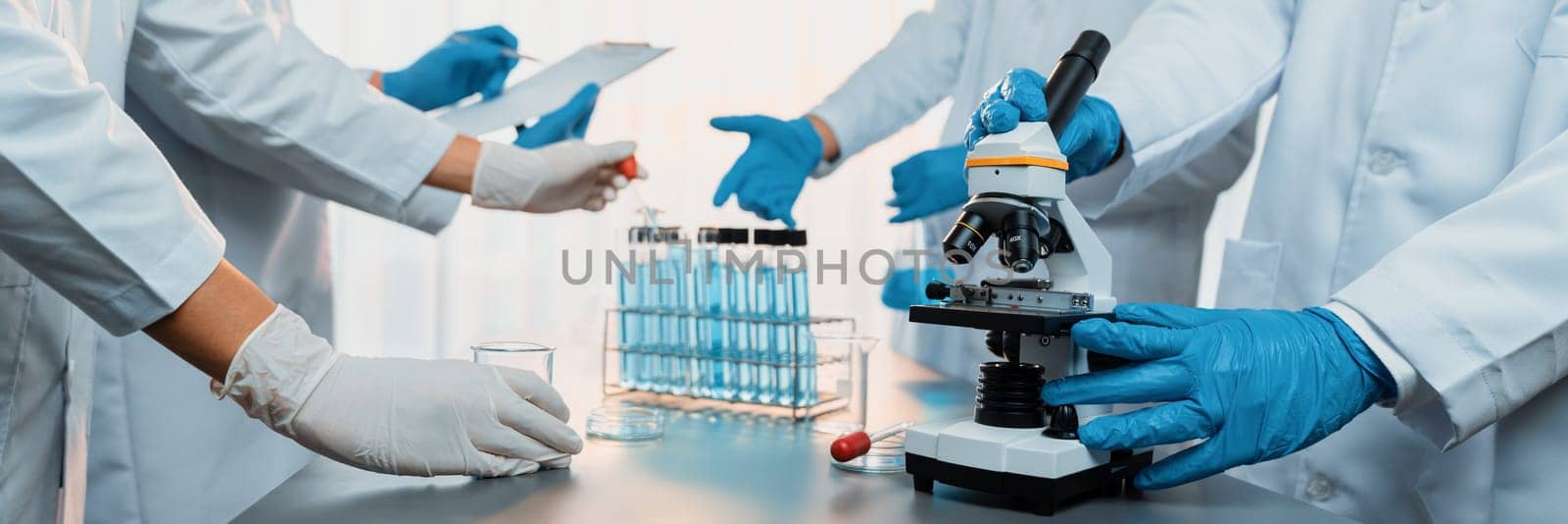 Group of dedicated scientist conduct chemical experiment using microscope in medical laboratory to develop new vaccine drug or antibiotic. Biotechnology lab and medicine research concept. Neoteric