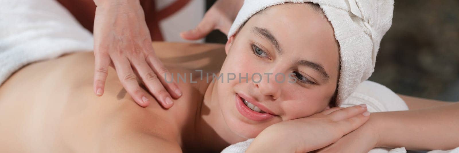 Beautiful young woman received a back massage on a spa bed from professional masseuse. Attractive female relaxes deeply by skilled hands of the massage therapist. Surrounded with nature. Tranquility.