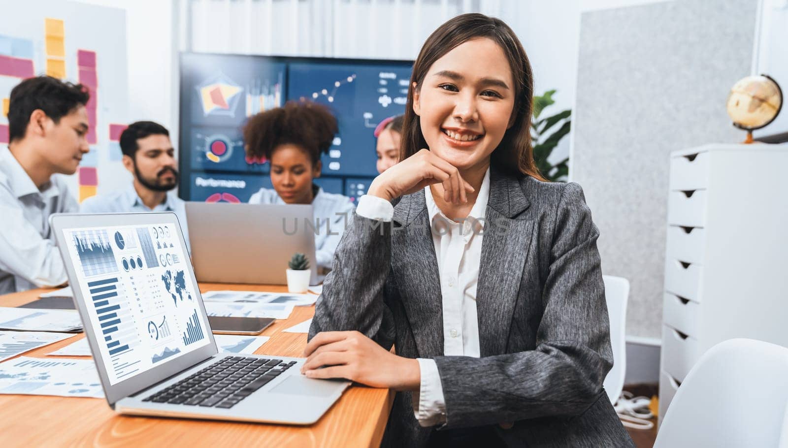 Portrait of happy young asian businesswoman with group of office worker on meeting with screen display business dashboard in background. Confident office lady at team meeting. Concord