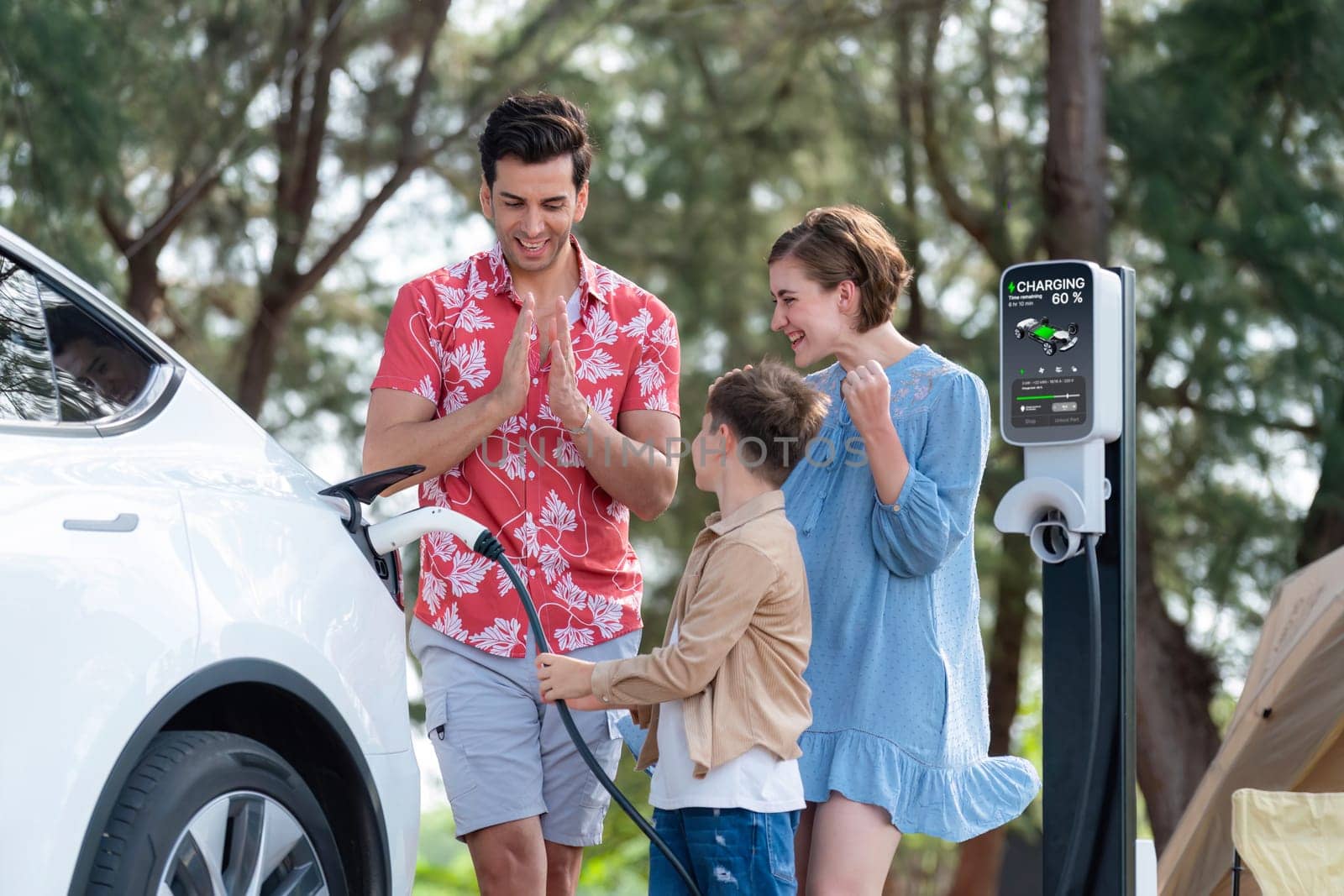 Outdoor adventure and family vacation camping in nature travel by eco friendly car for sustainable future. Lovely family recharge EV car with EV charging station in campsite. Perpetual