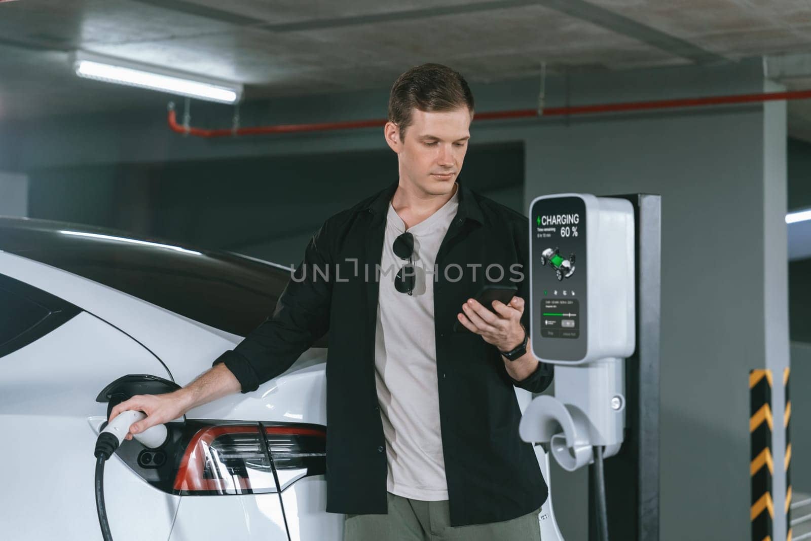 Young man travel with EV electric car to shopping center parking lot charging in downtown city showing urban sustainability lifestyle by green clean rechargeable energy of electric vehicle innards