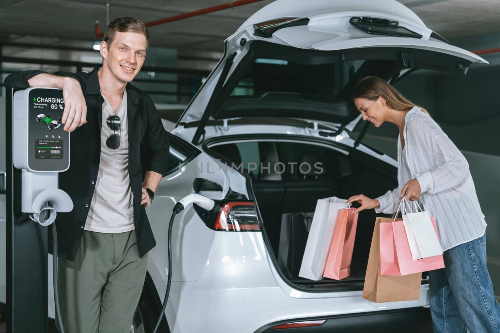 Young couple travel with EV electric car to shopping center parking lot charging in downtown city showing urban sustainability lifestyle by green clean rechargeable energy of electric vehicle innards