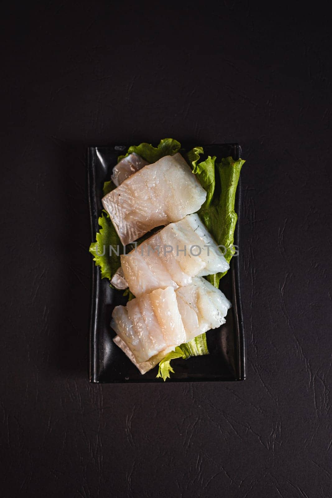 beautiful pike perch fillet on a green salad list on a black plate. View from above. Chinese cuisine, hotpot ingredient by tewolf