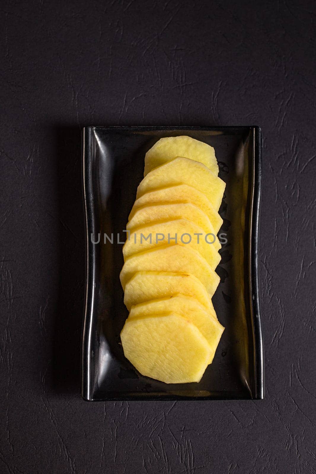 potato slices on a black plate. View from above. Chinese cuisine, ingredient for hotpot by tewolf