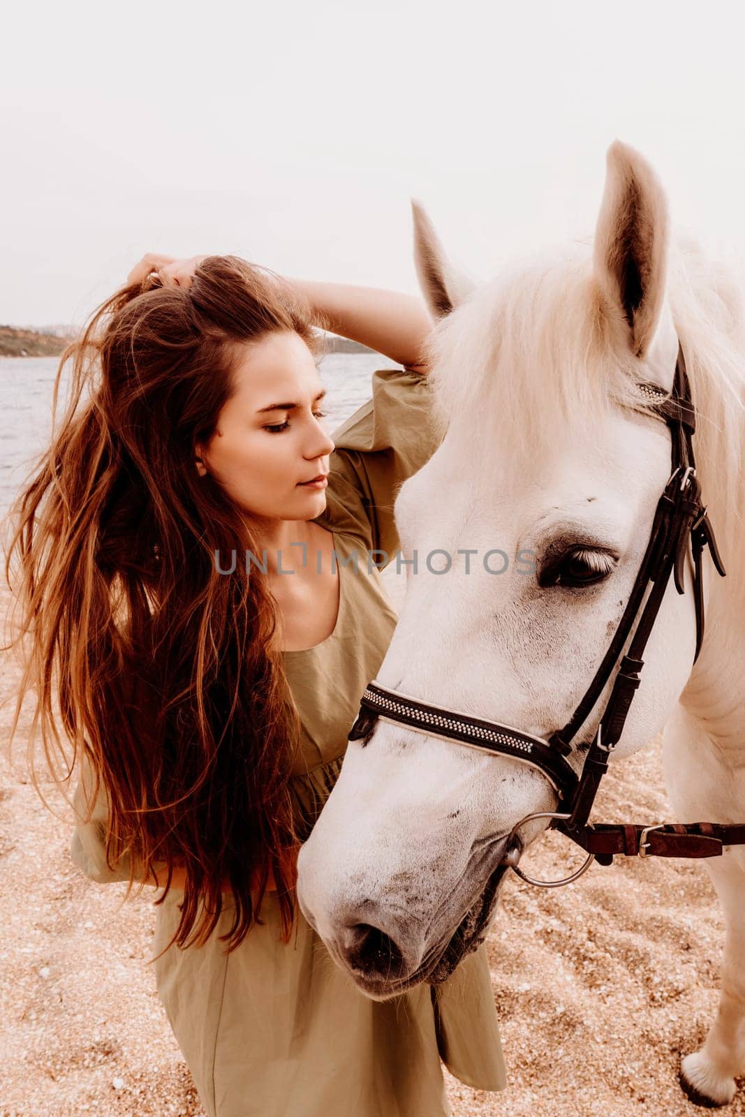 A white horse and a woman in a dress stand on a beach, with the sky and sea creating a picturesque backdrop for the scene