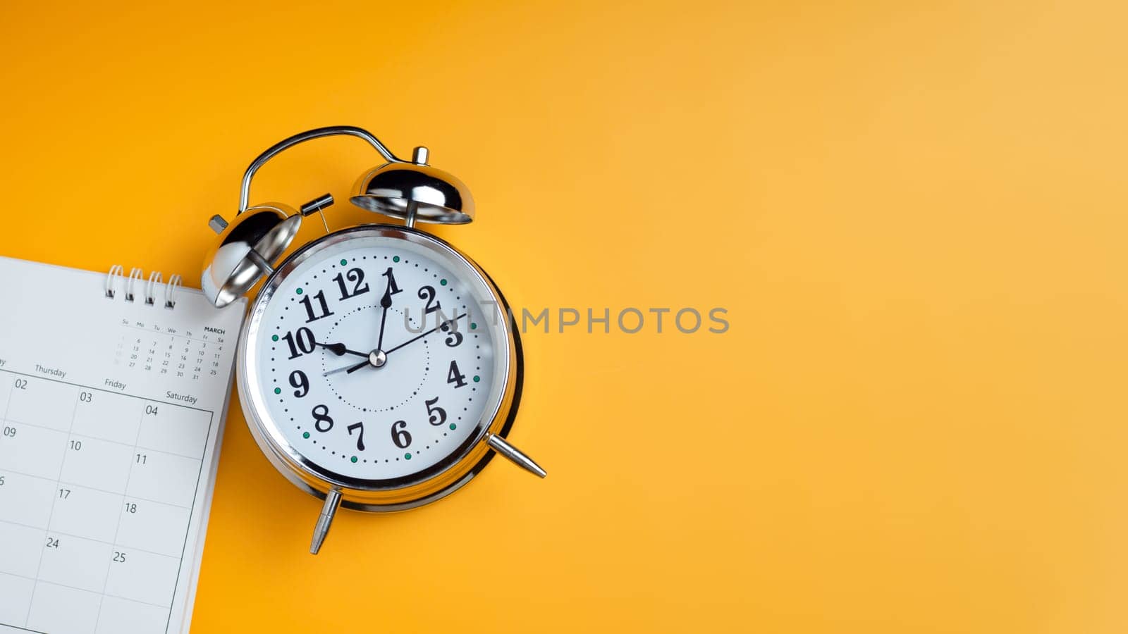 Top view of calendar and alarm clock on yellow background, planning for business meeting or travel planning concept by Unimages2527