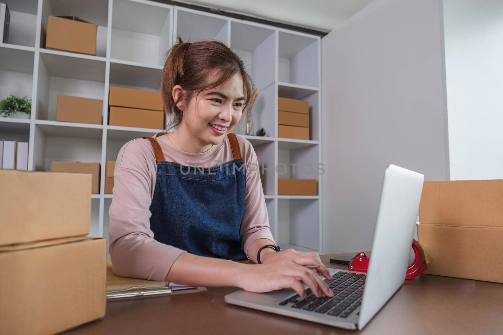 Happy young Asian woman entrepreneur, Smile for sales success after checking order from online shopping store in laptop at home office, Concept of merchant business online and eCommerce by wichayada