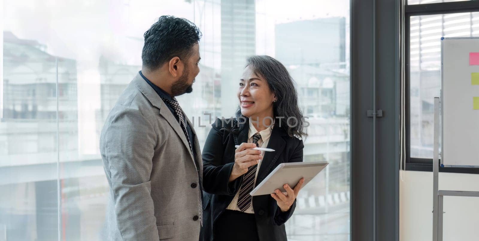 Entrepreneur Asian businessman and businesswoman discussing new business project in tablet in modern Meeting In Modern Office, Asian business casual concept. by wichayada