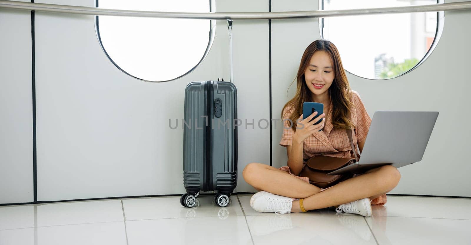 Happy woman texting on her mobile phone and waiting for her boarding gate to open at the airport terminal. Tourist journey trip concept