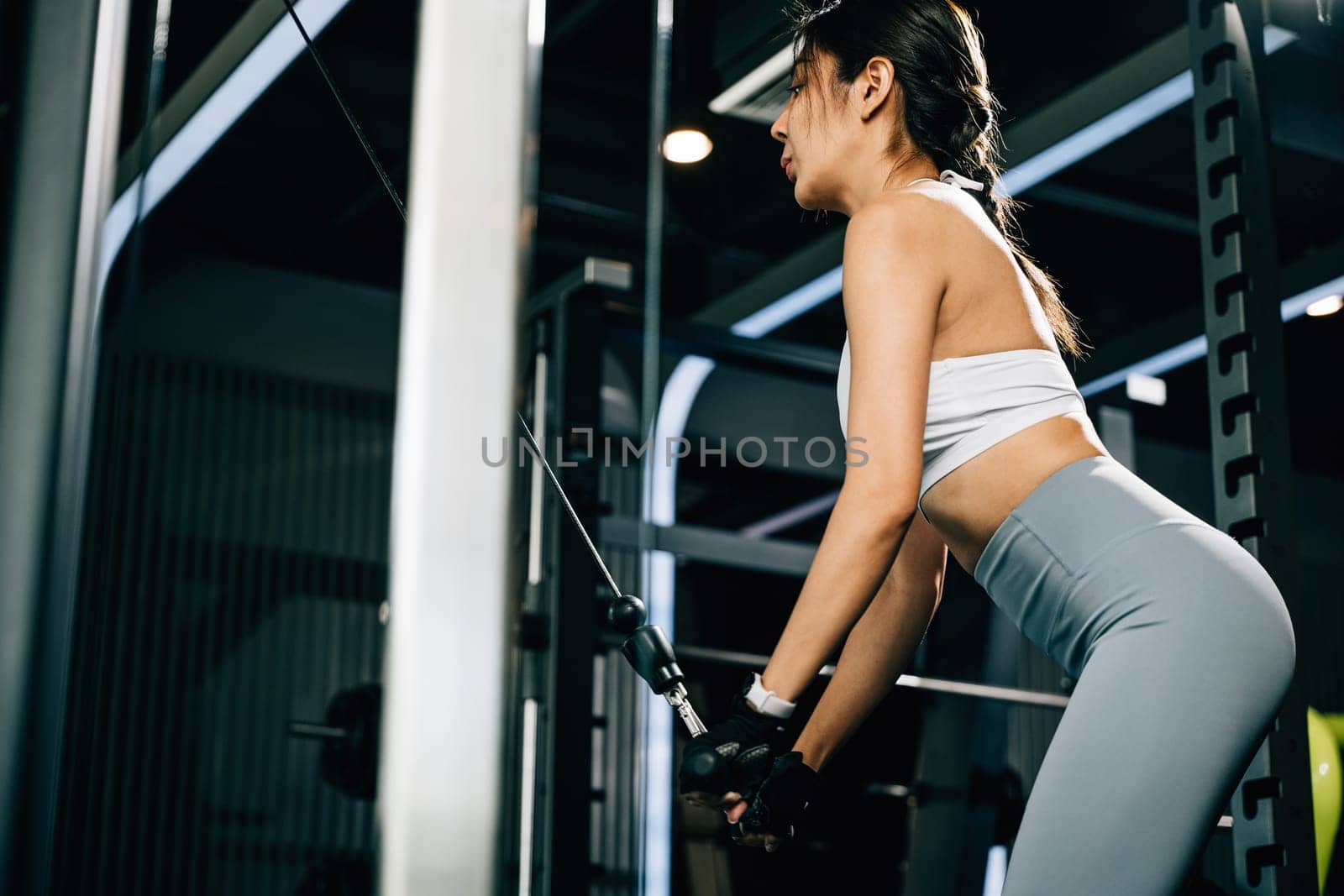 Woman holding onto the bar of a weight machine, using her arm strength to pull down and workout her muscles. fitness center health workout concept